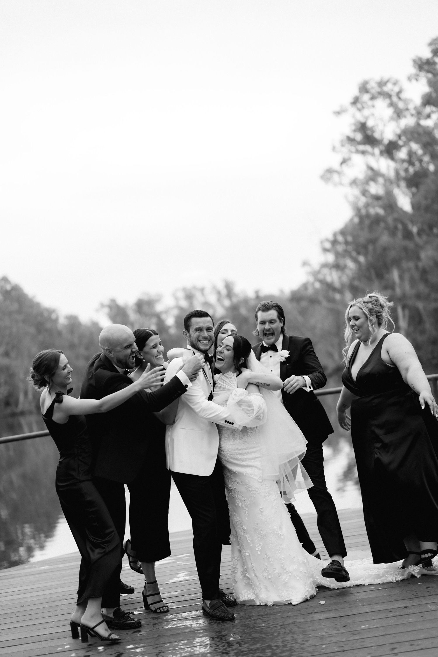 Black and white photo of wedding party doing synchronized leaning pose on outdoor deck.