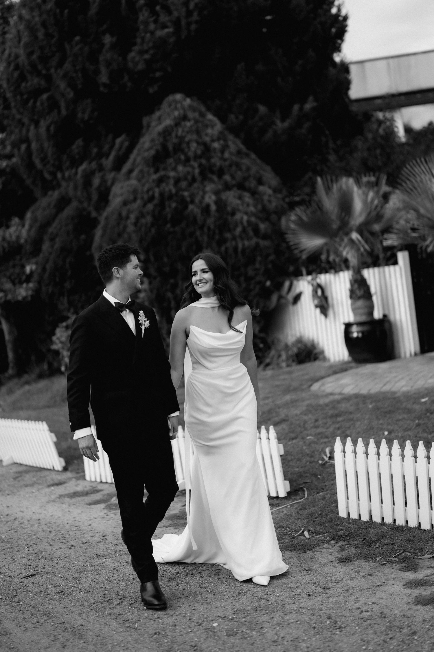 Black and white photo of a couple walking along a white picket fence pathway.