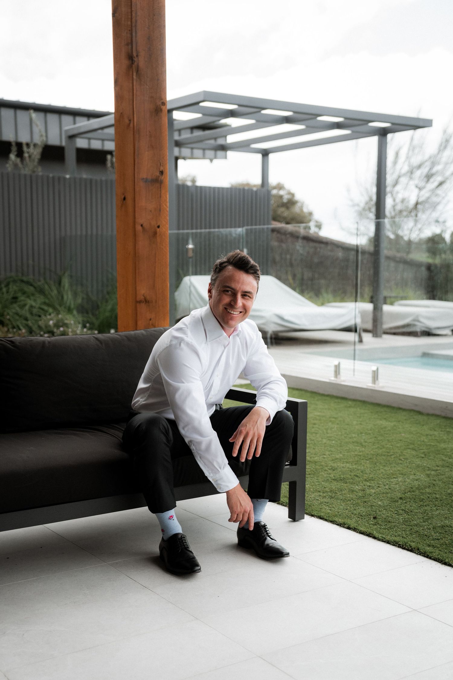 A person in a white dress shirt sits casually on modern outdoor furniture near a swimming pool.