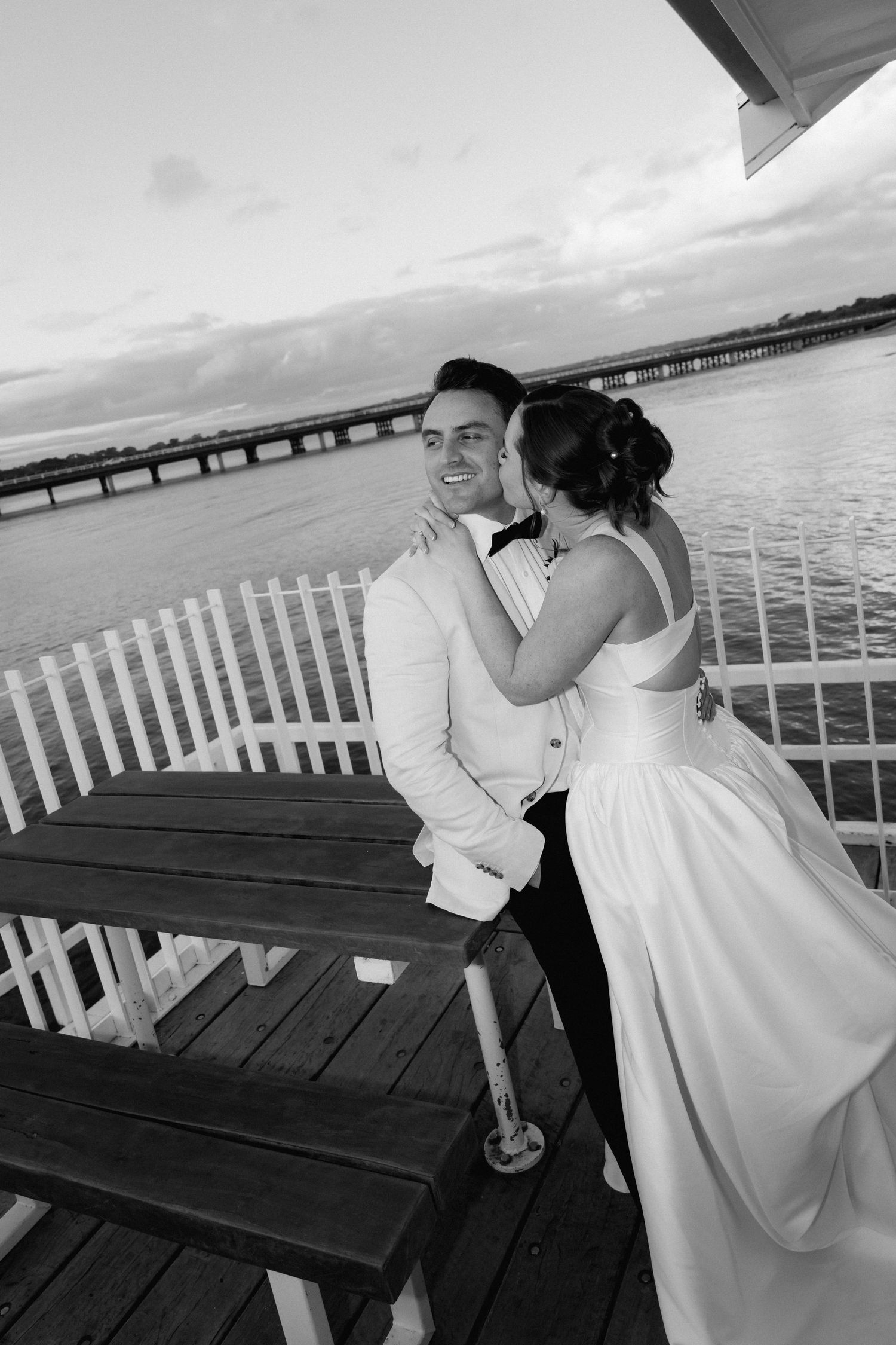 Couple shares intimate moments on a wooden pier overlooking the ocean at sunset.