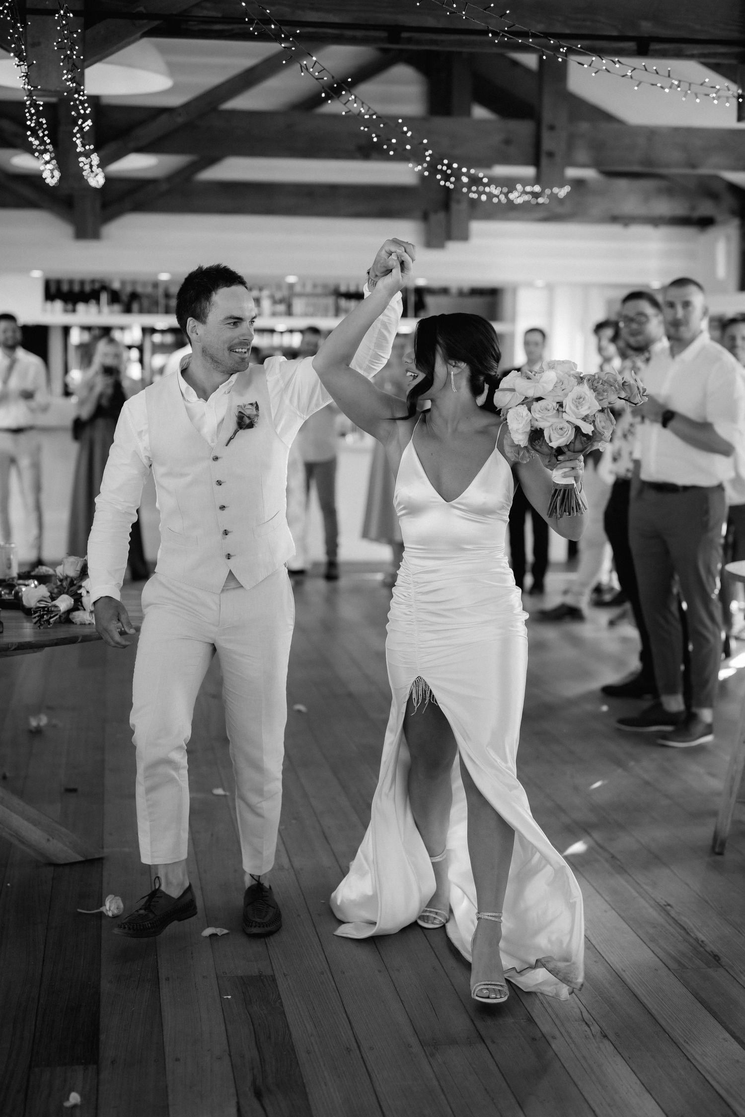 Wedding guests dance on a rustic wooden floor during a celebration.