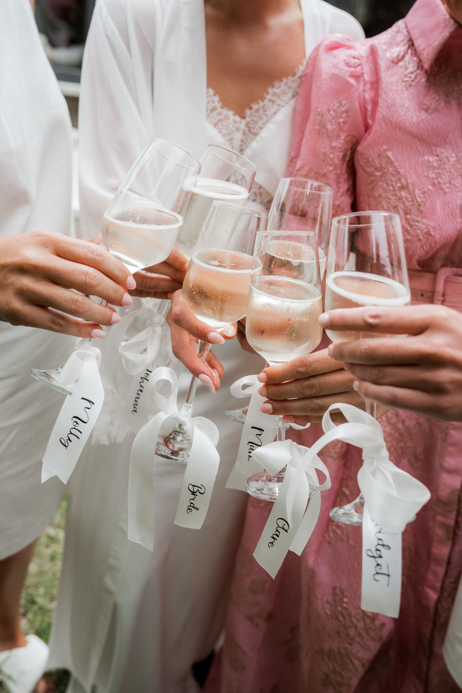 Bridesmaids in pink and white robes toasting with champagne glasses tagged with personalized name ribbons.