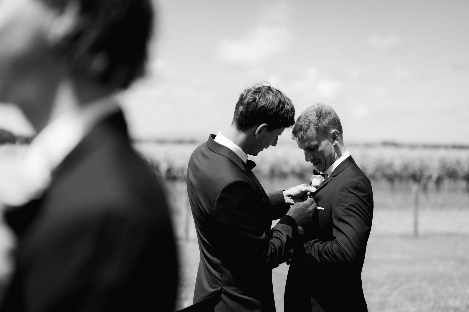 Black and white candid wedding moments show emotional embraces between wedding party members during outdoor celebration.