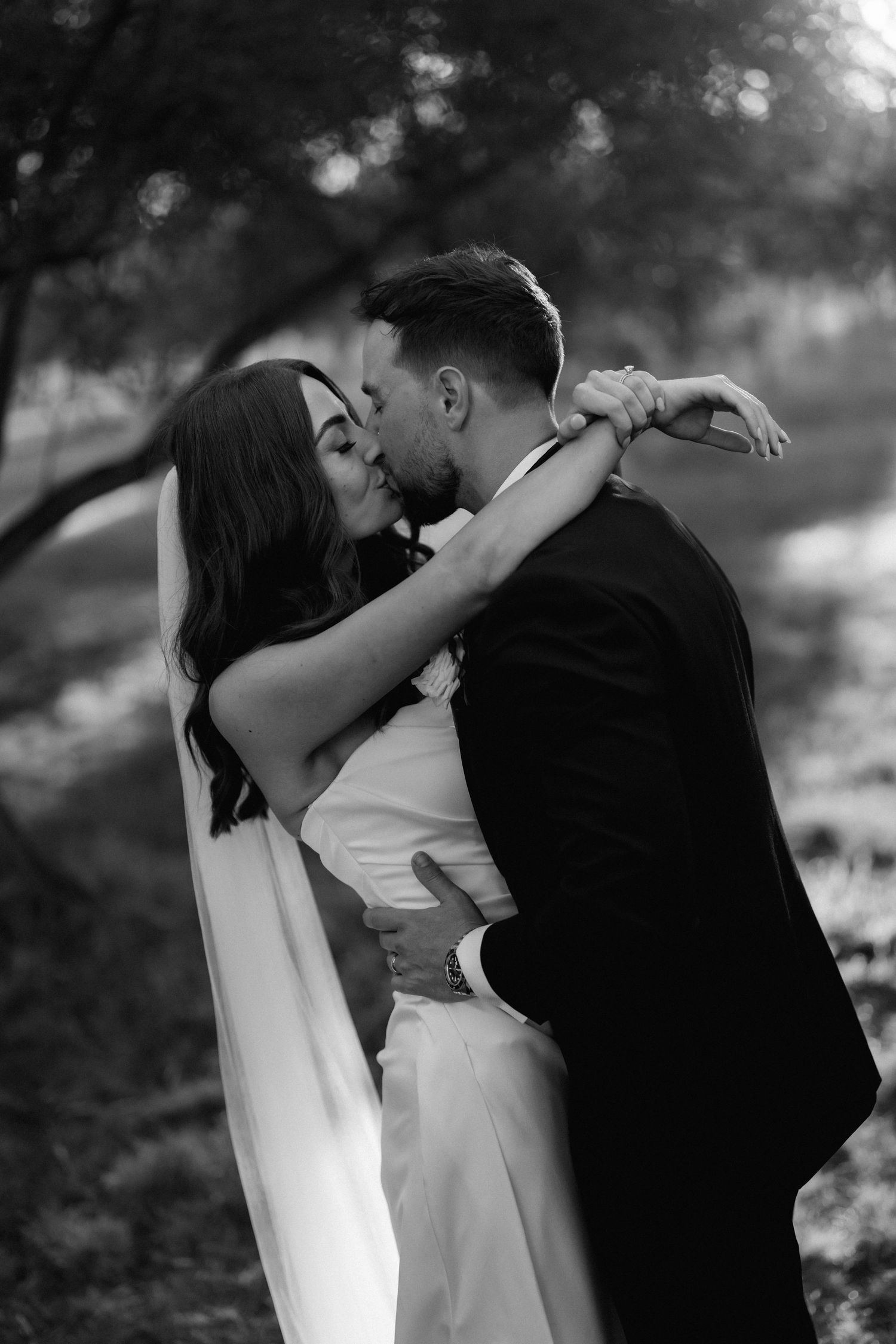 A romantic black and white wedding portrait captured in soft natural lighting outdoors.
