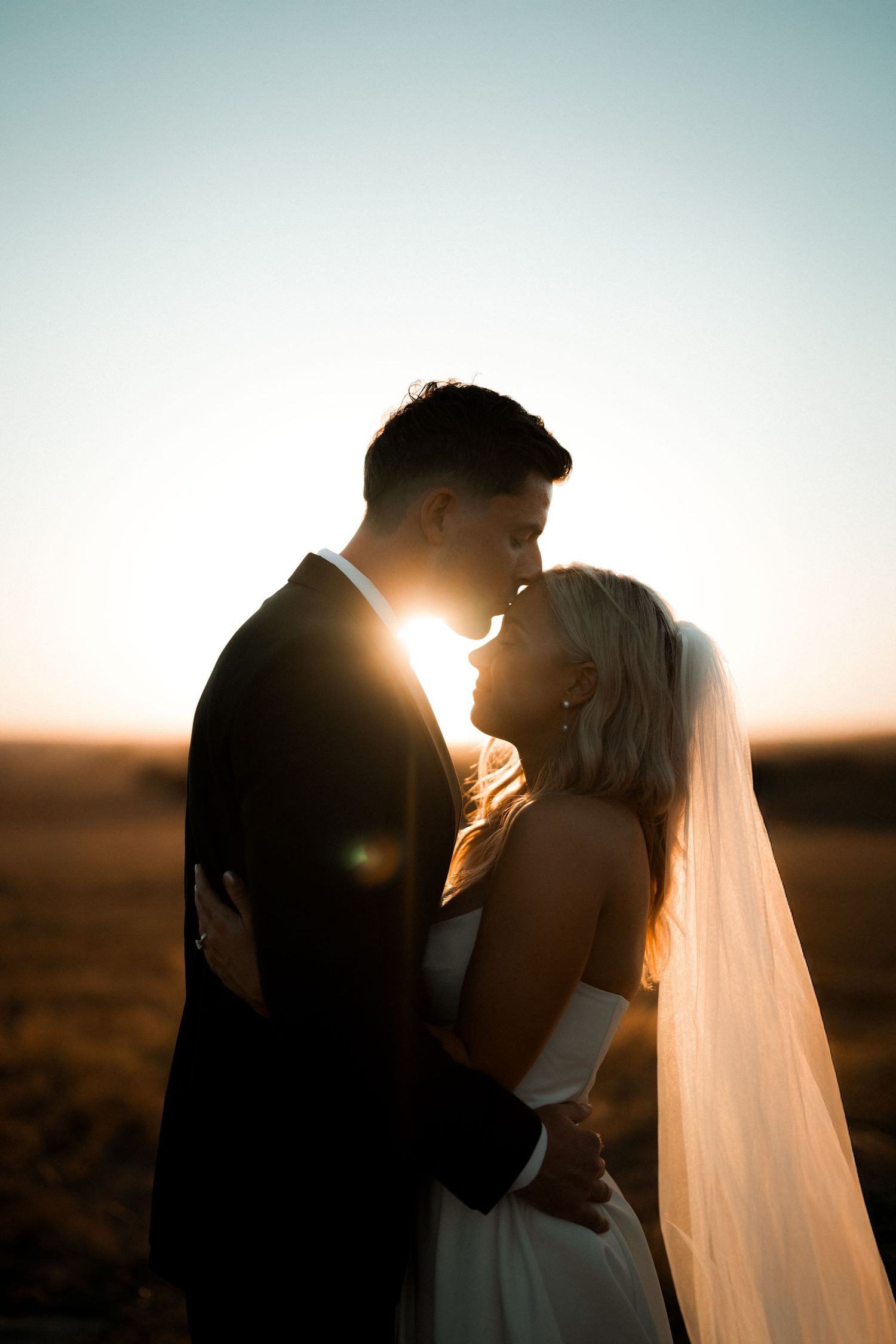 A romantic silhouette of a couple sharing an intimate moment at sunset with a flowing bridal veil.