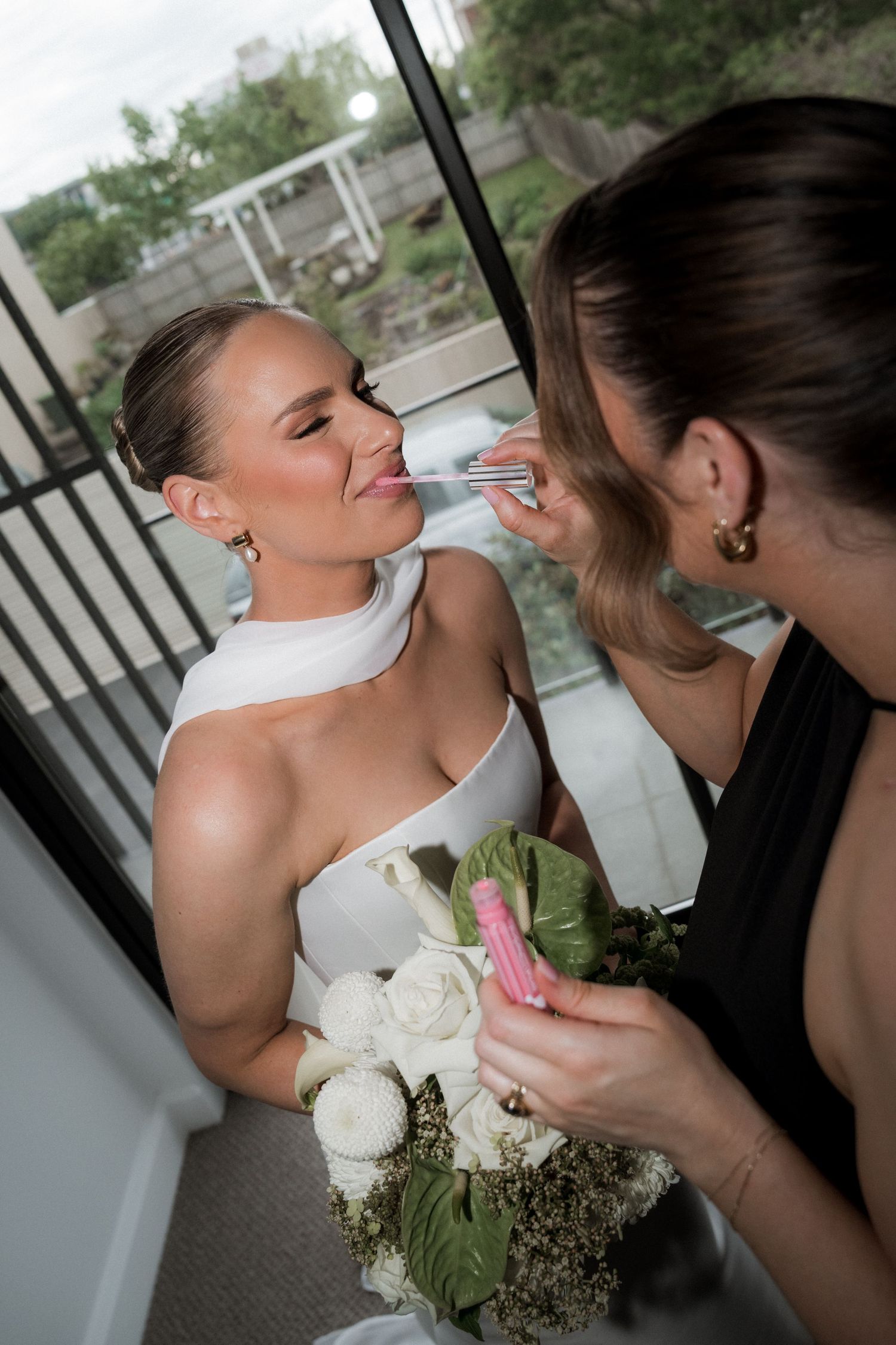 Bride holding white roses while getting ready with assistance on wedding day.