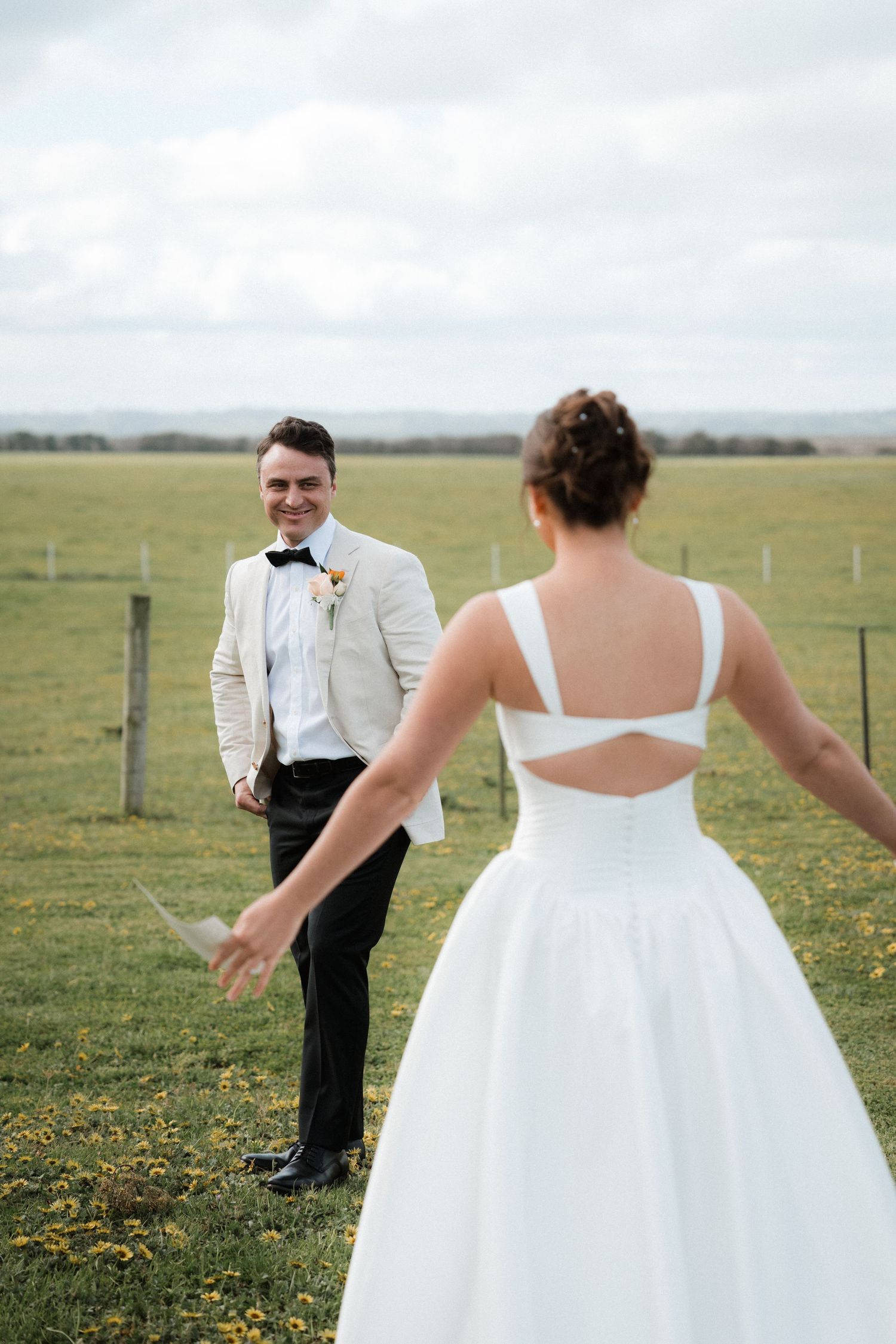 First look wedding moment in a sunny meadow with yellow wildflowers.