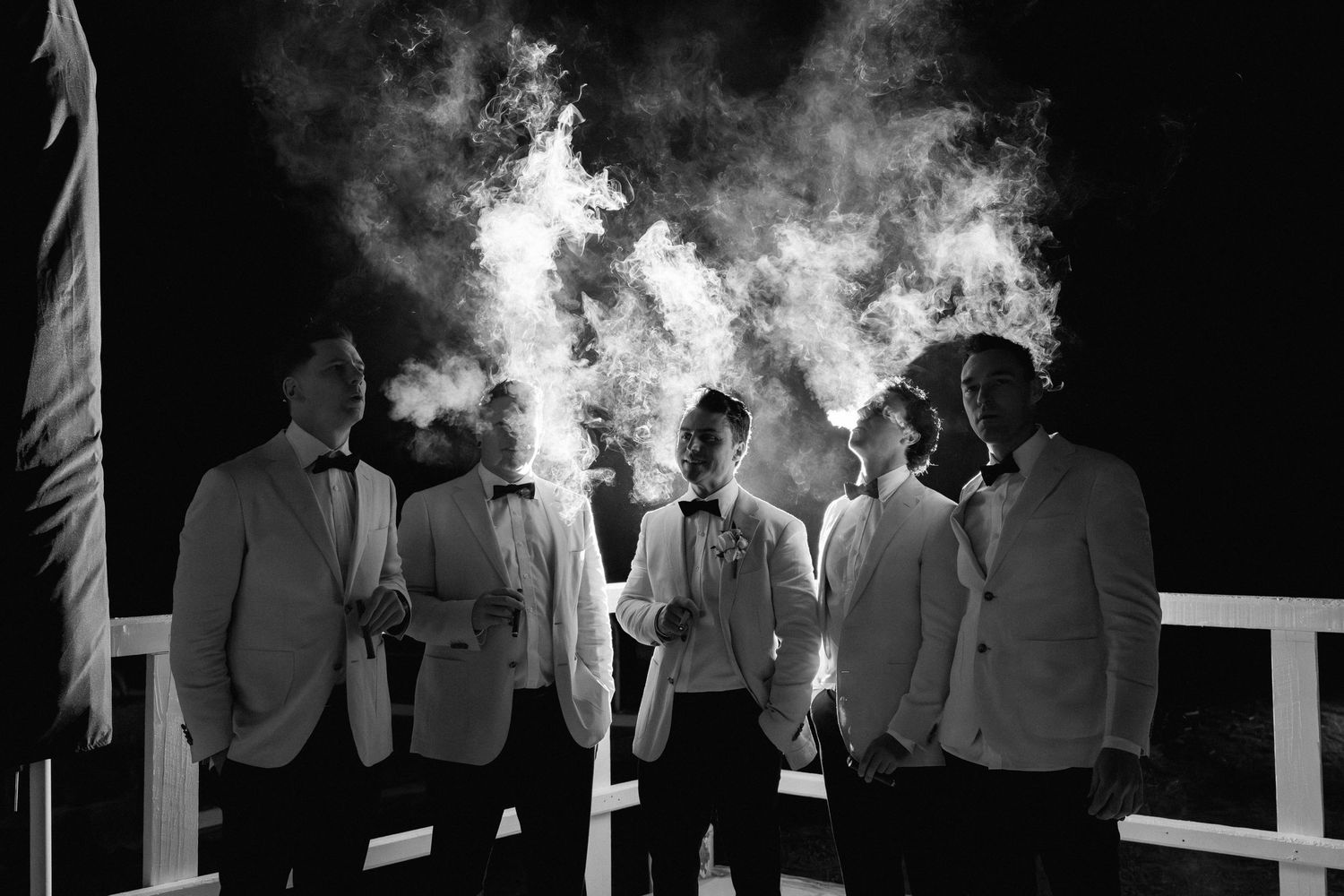 Silhouetted wedding party members against a smoky background outdoors.