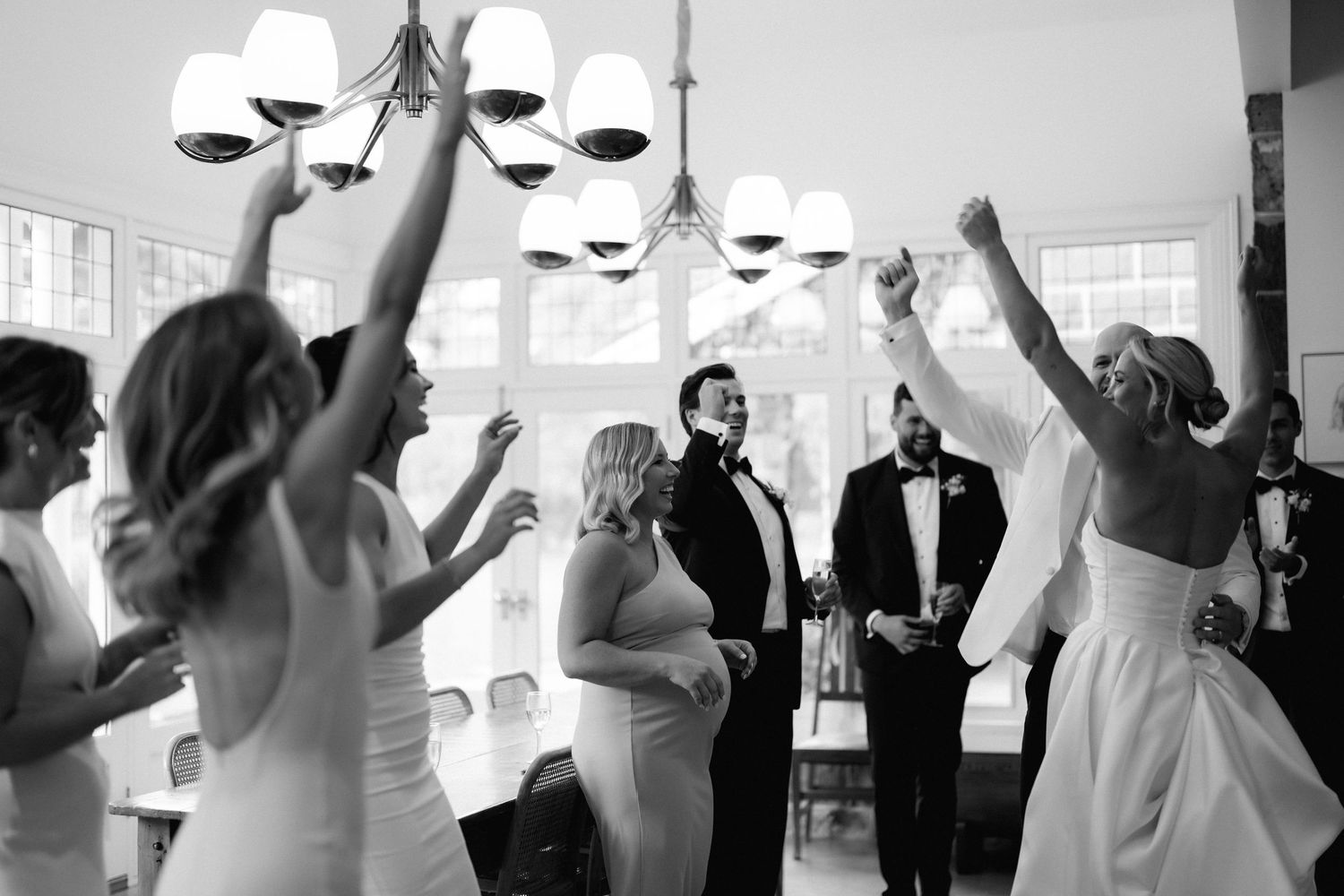 Wedding guests dance with hands raised during a festive black and white celebration in an elegant reception hall.