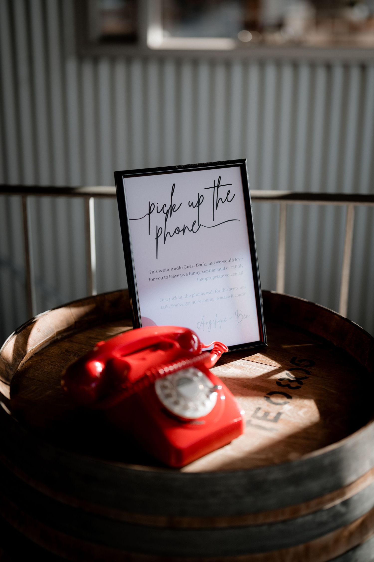 A vintage red rotary telephone sits on a wooden barrel next to a 'Pick Up the Phone' sign.