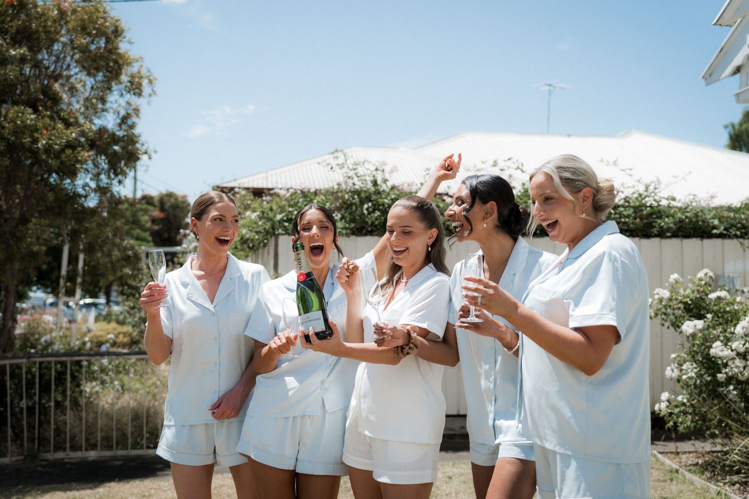 A group wearing matching white outfits celebrating outdoors on a sunny day.