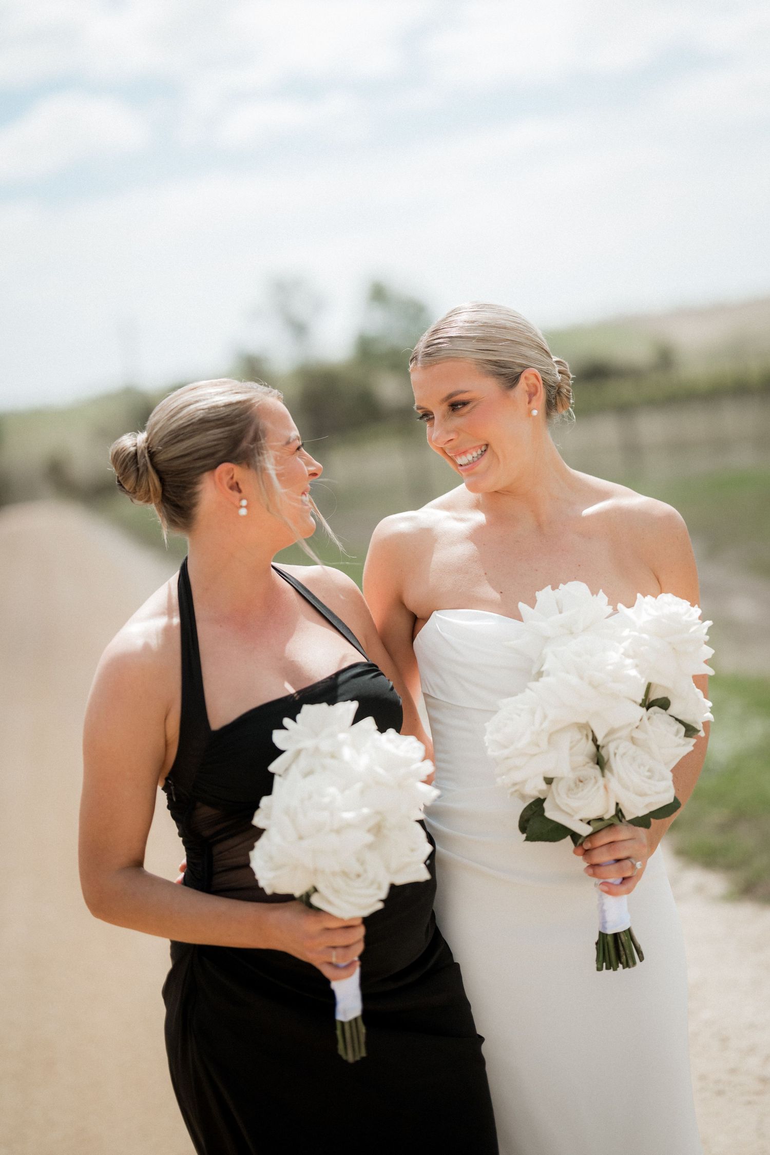 Wedding party members in black and white attire pose with bouquets of white flowers in outdoor setting.