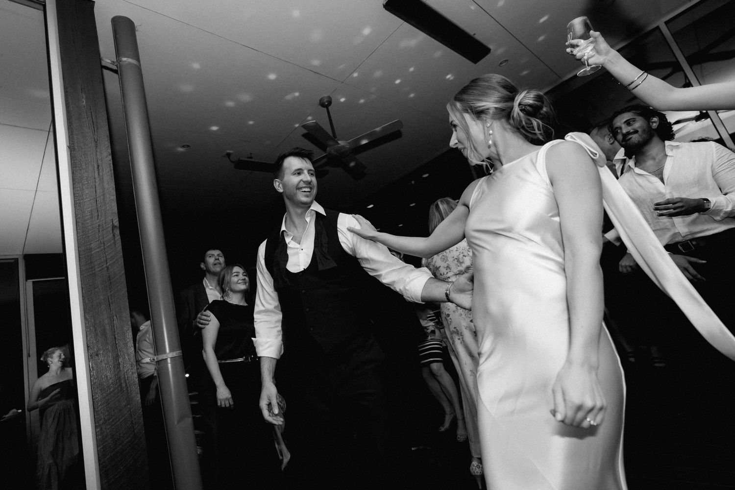 People dancing and celebrating at a wedding reception in a black and white photo.