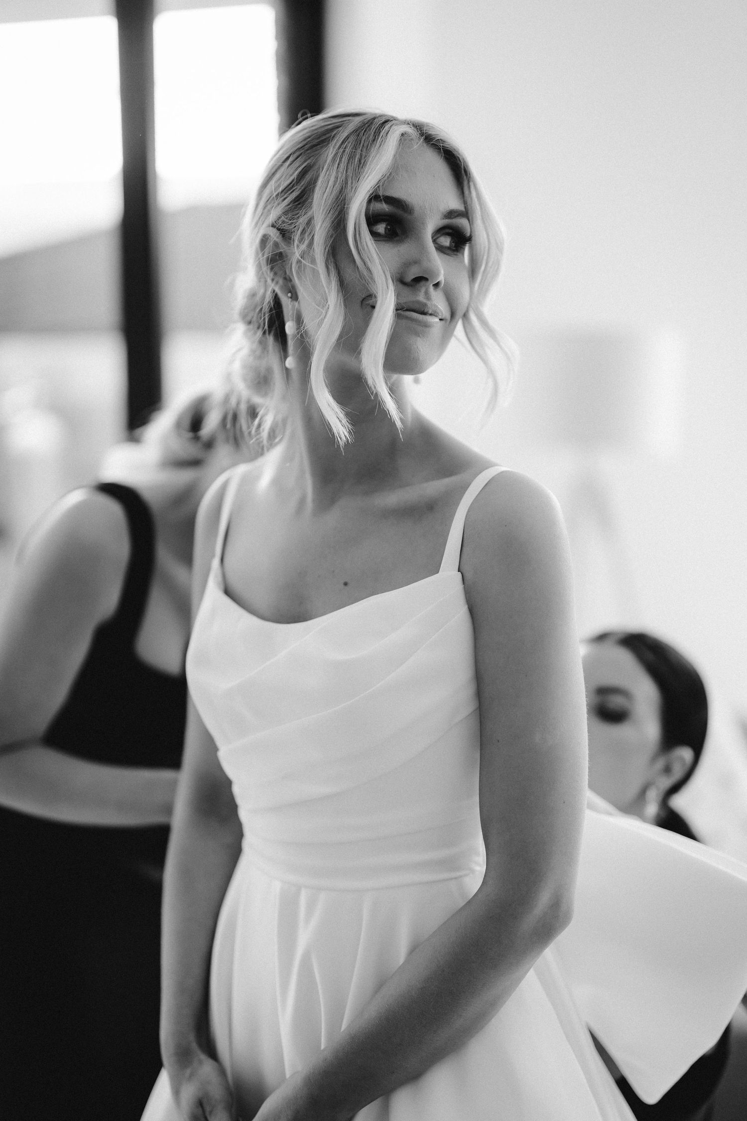 A bride in a classic white wedding gown smiles while getting ready before the ceremony in black and white.