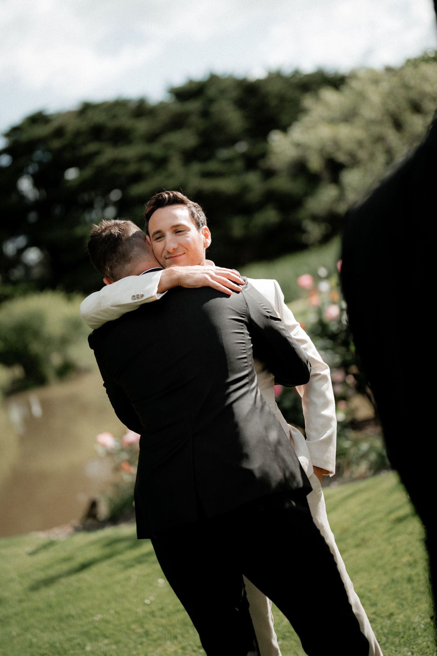 Two people share an emotional embrace on a grassy hillside during an outdoor celebration.