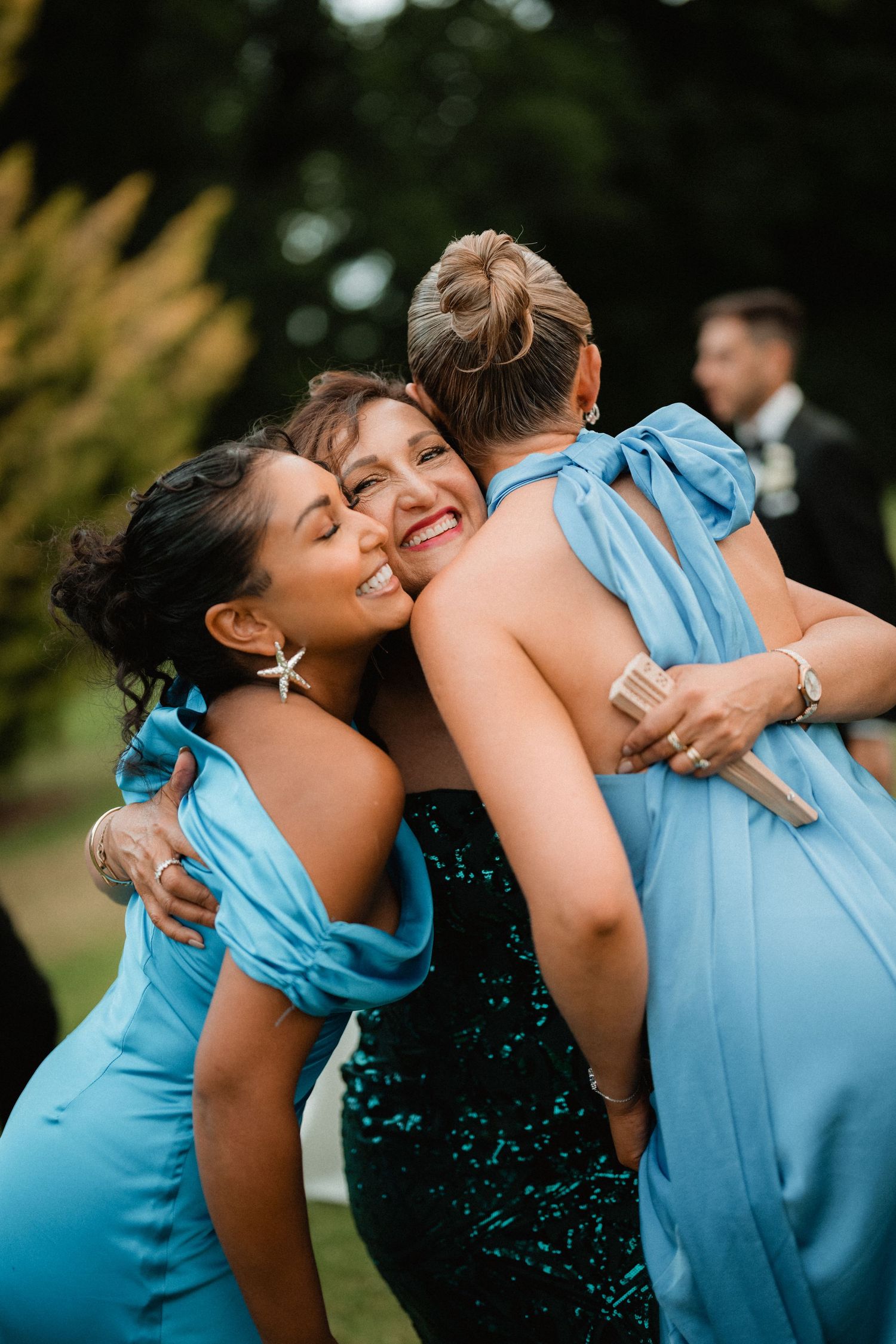 Wedding attendees in light blue dresses share a joyful group hug during outdoor celebration.