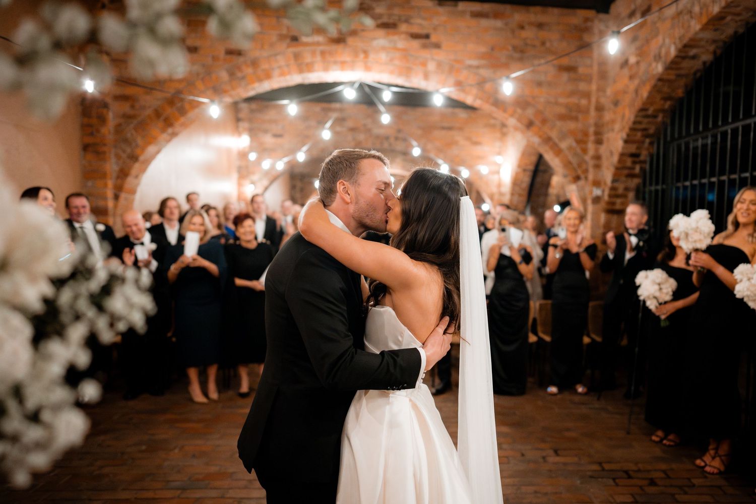 Wedding couple shares their first dance under romantic brick archways and twinkling lights.