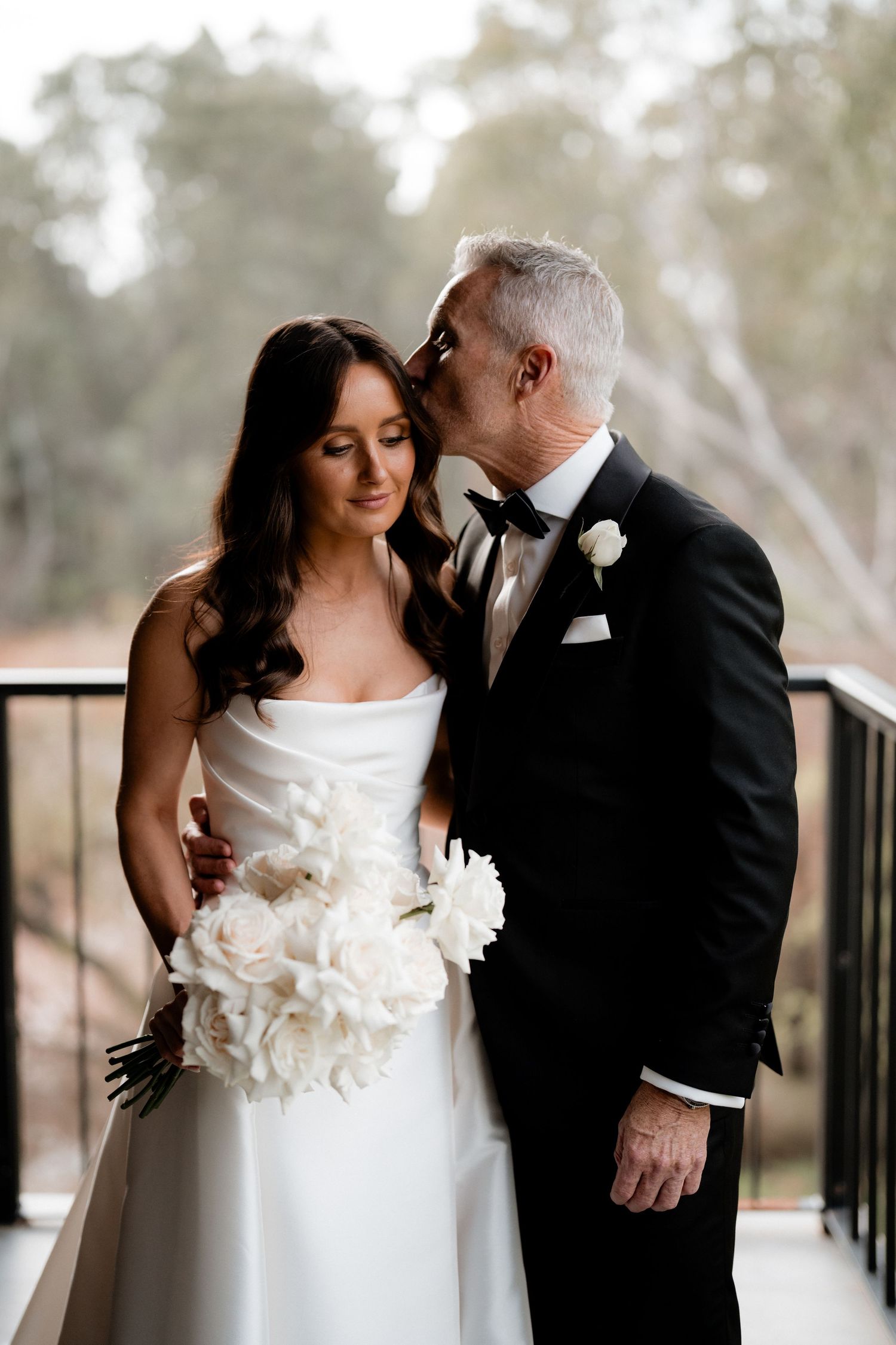 Intimate romantic moment between bride and groom in formal attire on outdoor balcony.