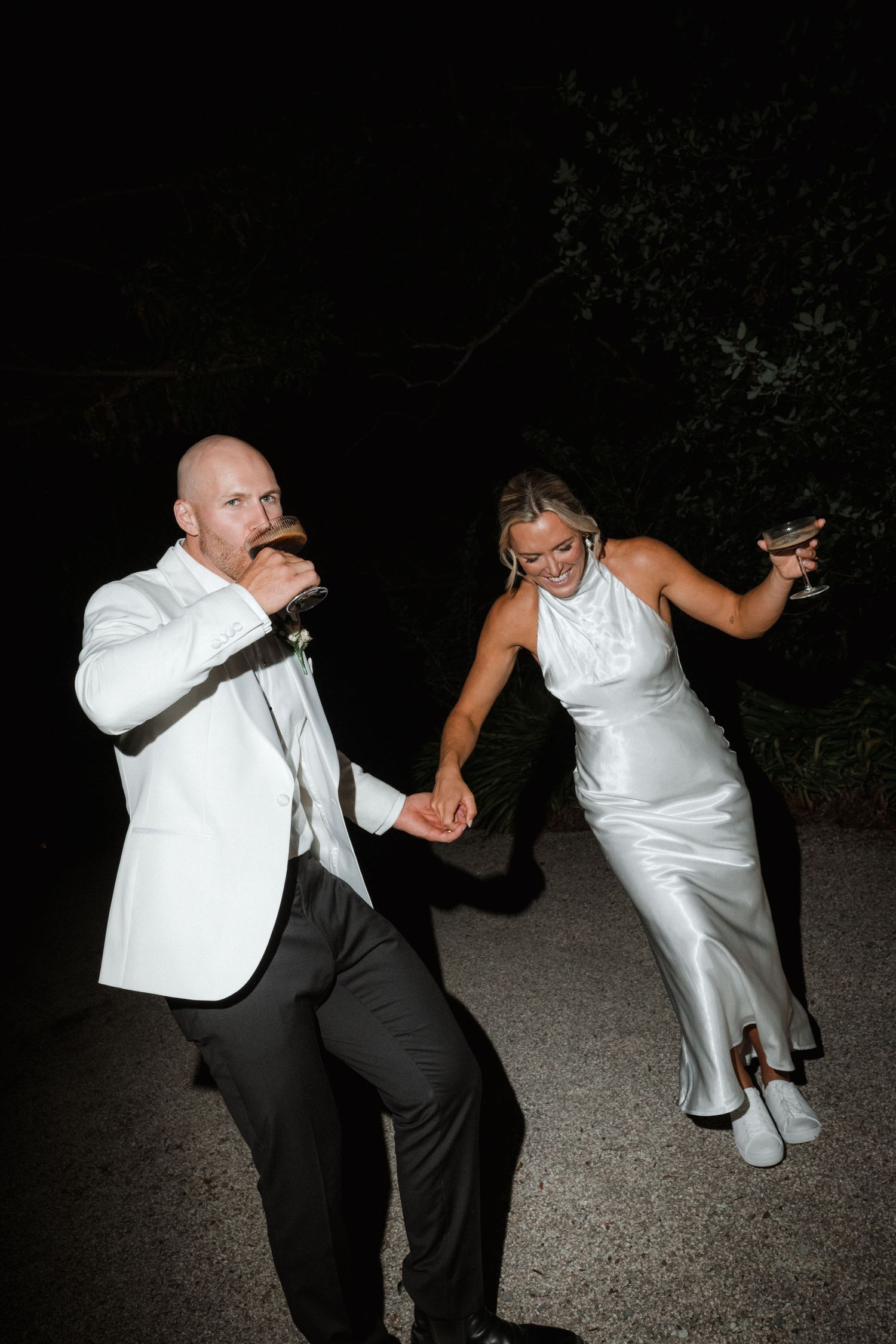 Couple in white formal wear dancing playfully at night.