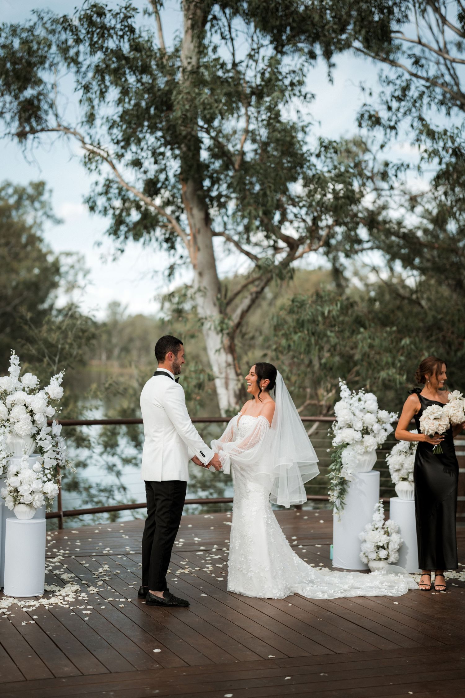 Wedding ceremony setup on a wooden deck with white floral arrangements and decorative columns.