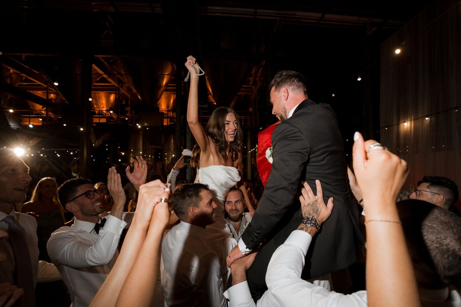 A crowd of people dancing with raised hands at a dark nightclub or party venue.
