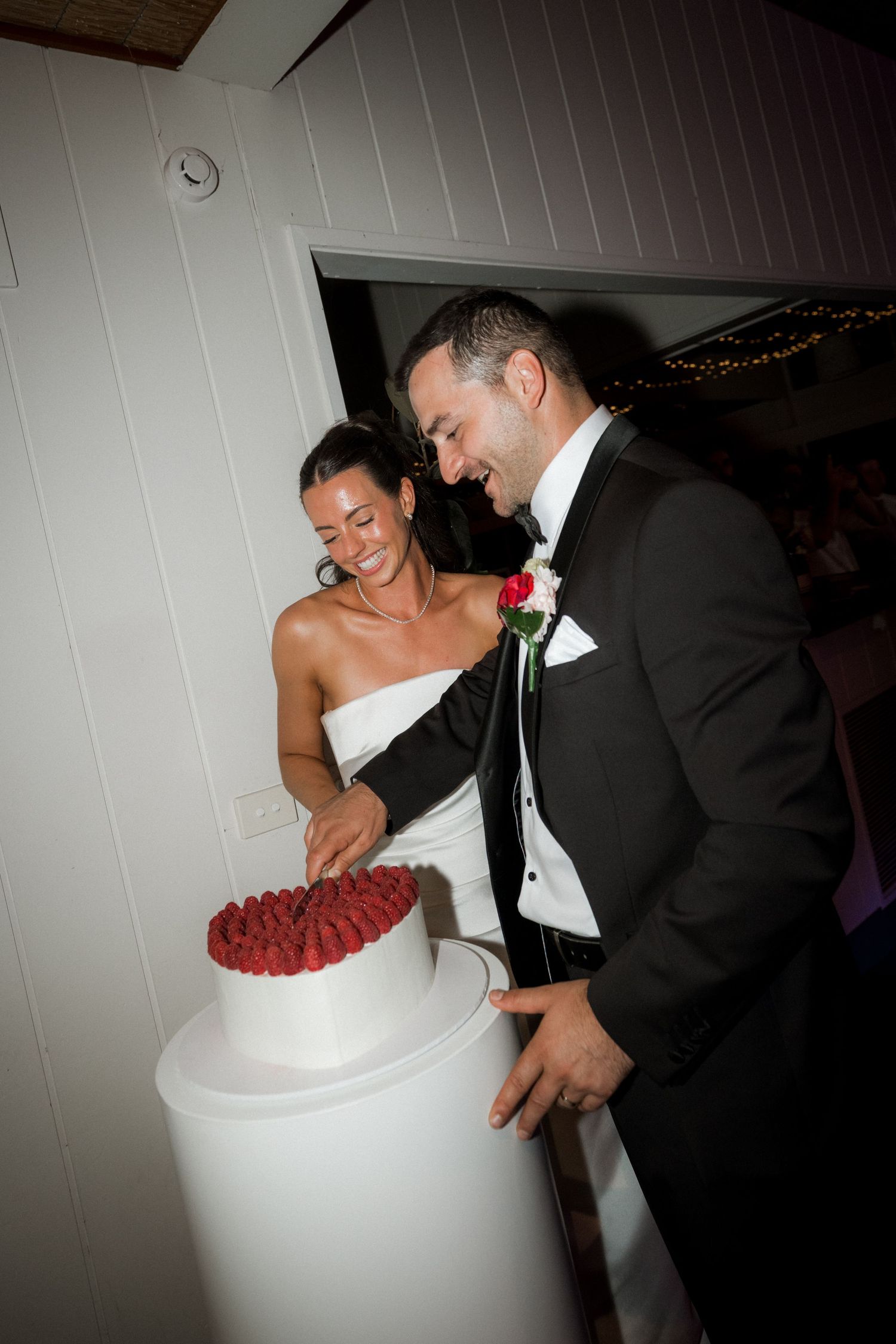 Couple cutting into their white wedding cake decorated with fresh raspberries during reception.
