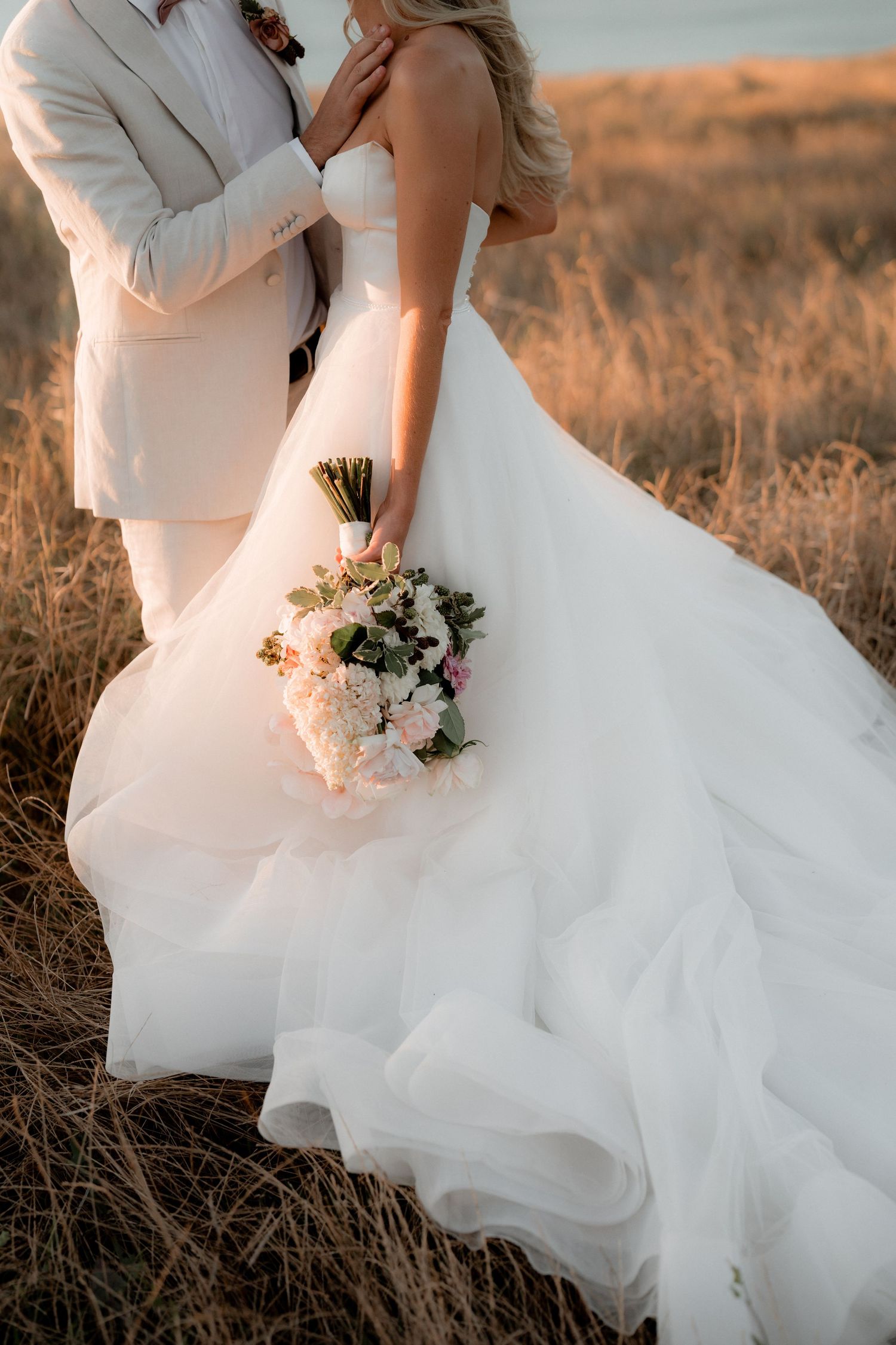 A dreamy wedding portrait featuring flowing white dress details at golden hour.