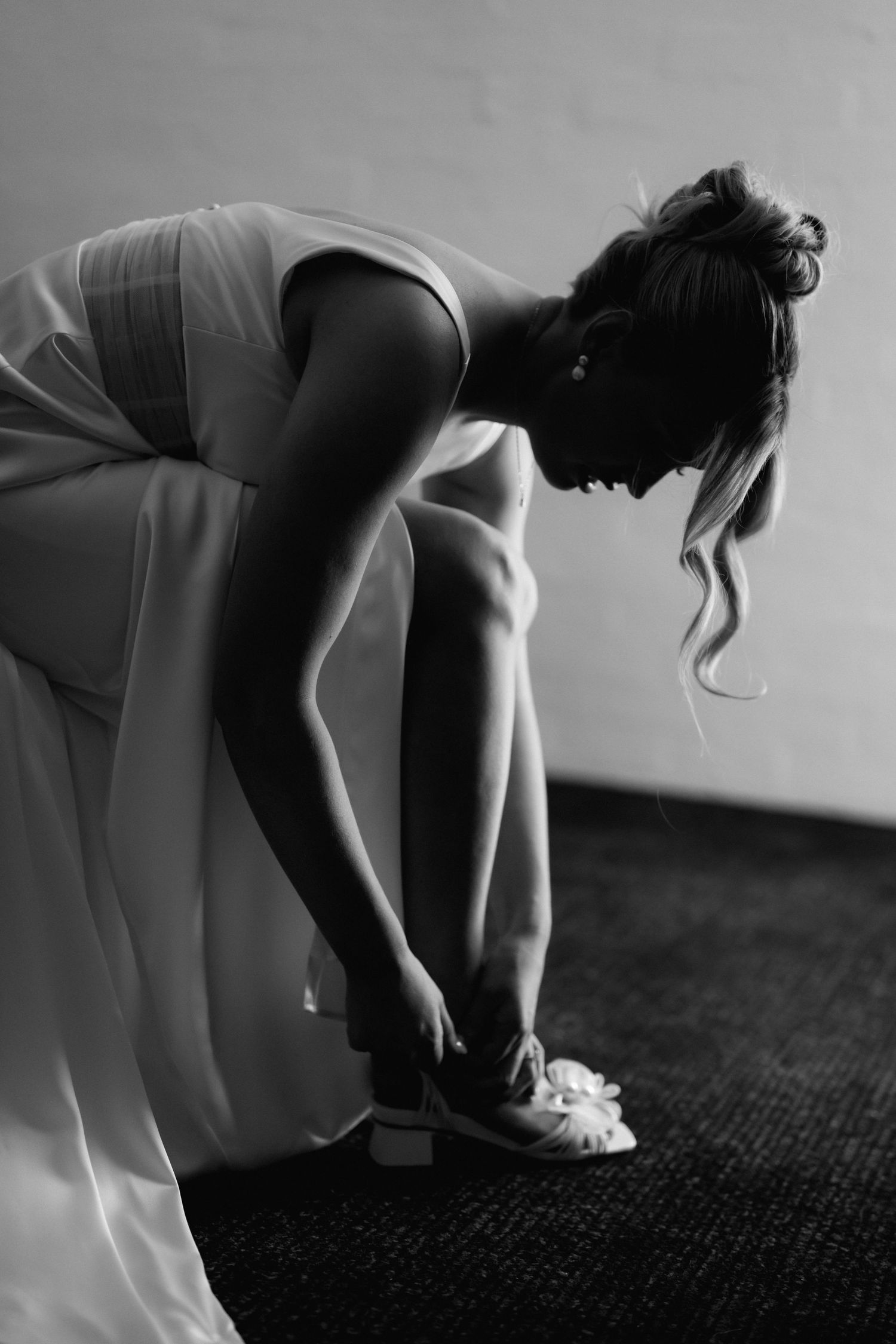 Artistic black and white shot of someone adjusting their shoe while wearing a flowing white dress.