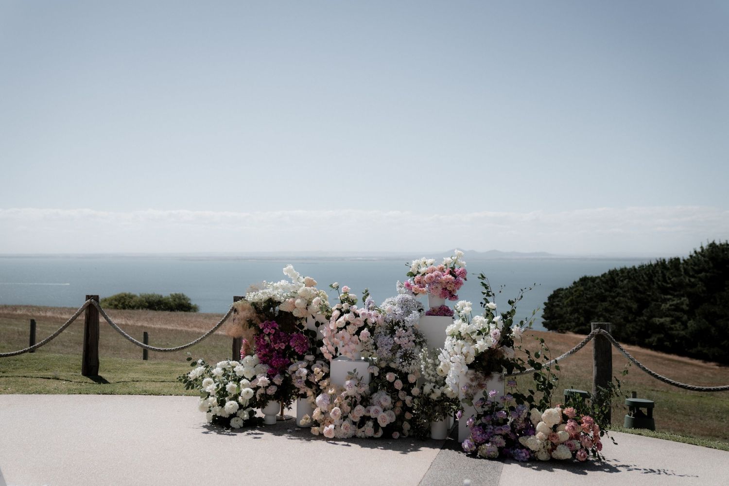 A floral arrangement with pink and white flowers sits on a railing overlooking the ocean on a misty day.
