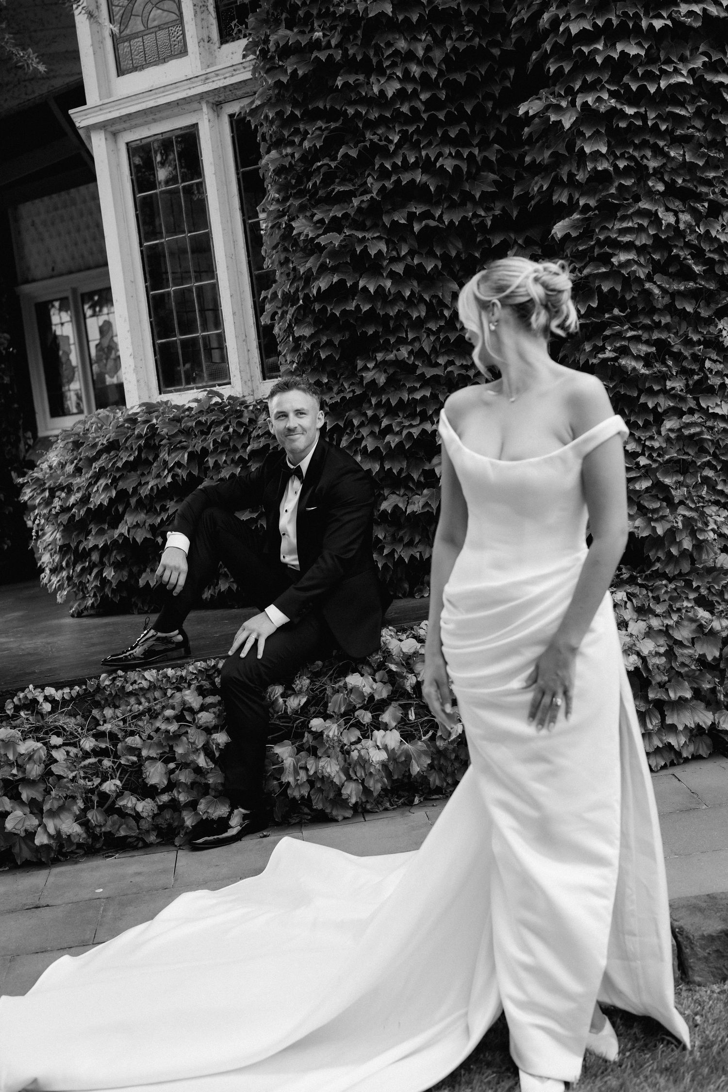Couple creates dynamic poses against ivy-covered wall in elegant wedding attire.