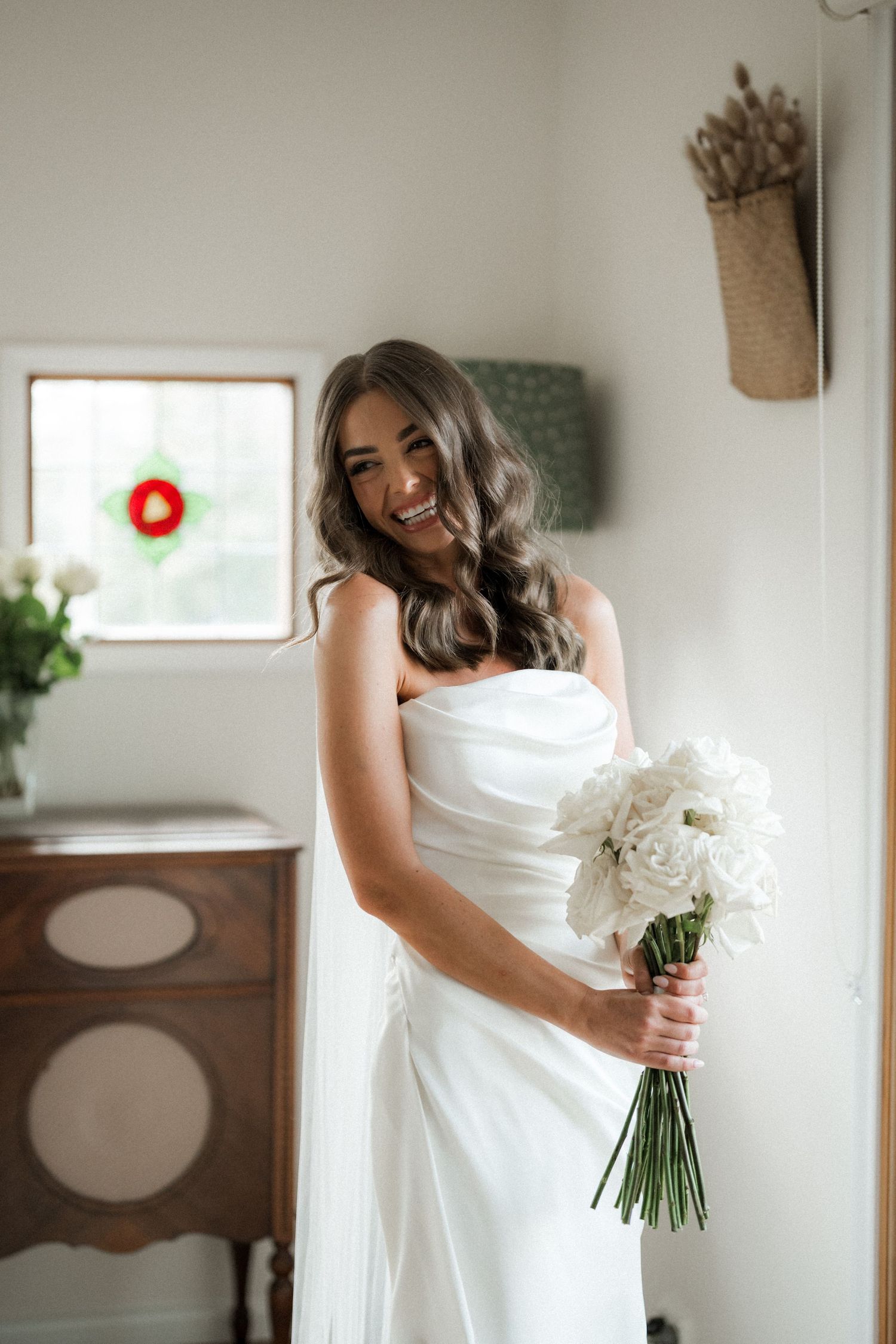 A bride in a classic white wedding dress holds a beautiful bouquet of white flowers in an indoor setting.