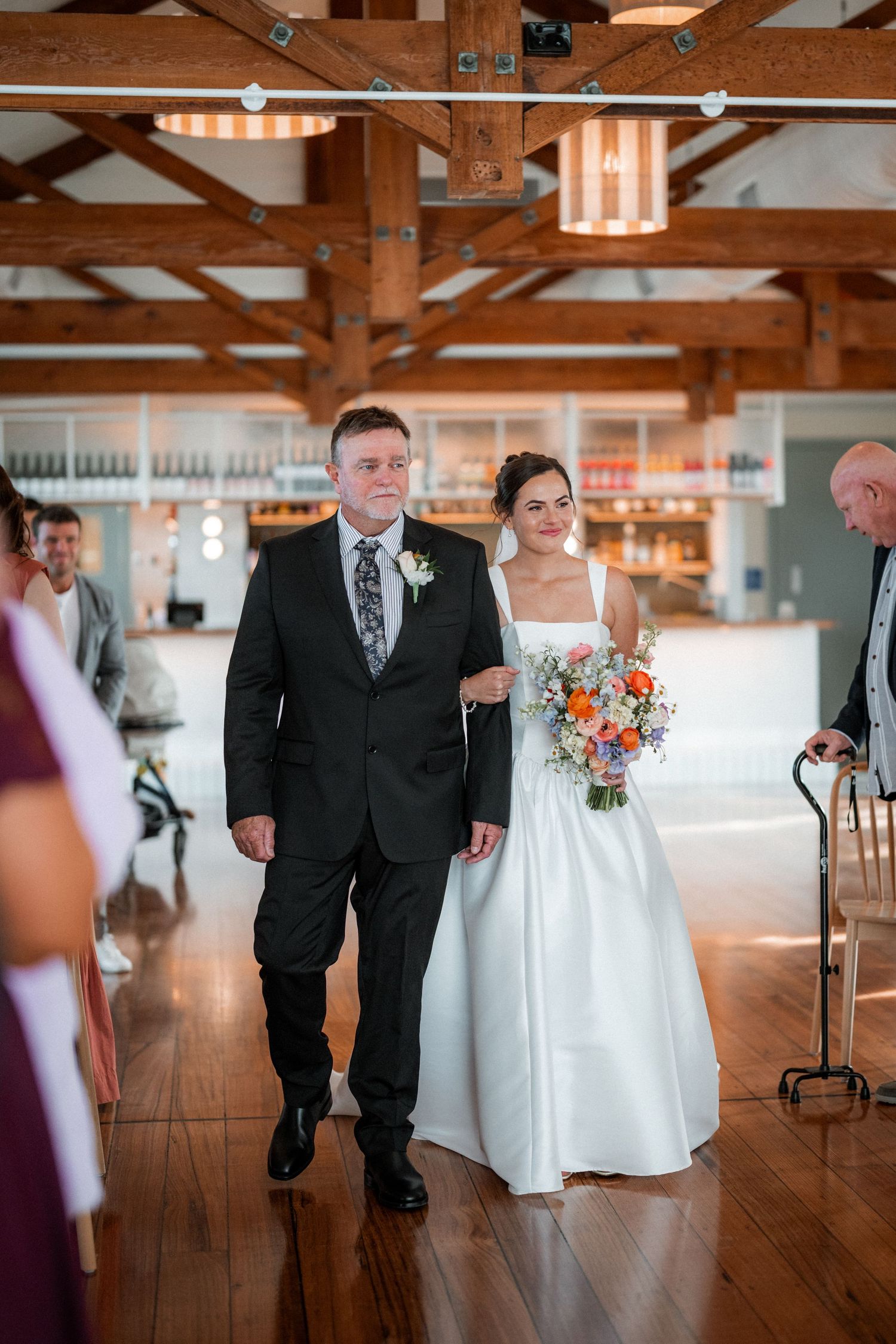 Wedding party walking across a rustic wooden floor venue with exposed beam ceilings.