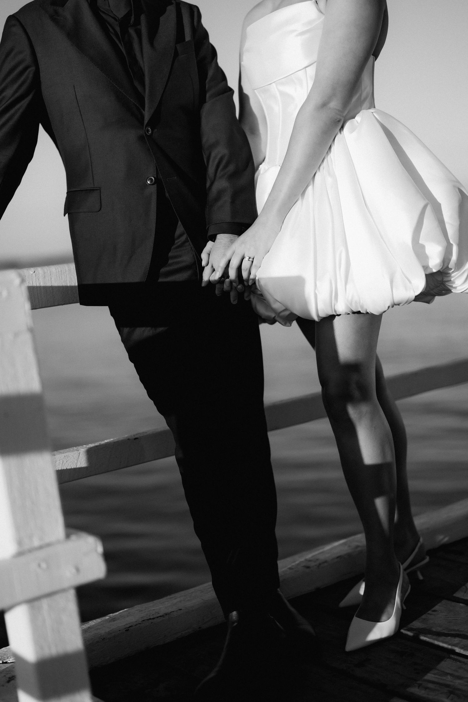 Black and white photo showing contrasting formal wedding attire details on a wooden deck.