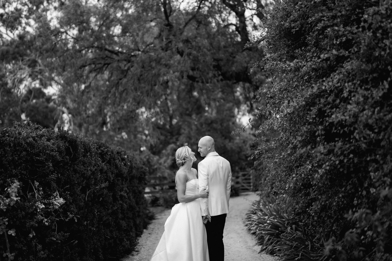 A romantic black and white photo of a couple on a garden path surrounded by lush greenery.