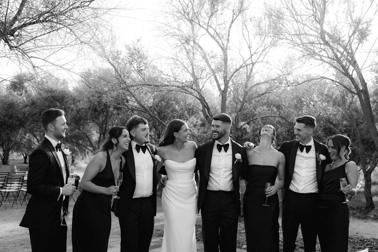 Wedding party poses together in black and white against a backdrop of trees.