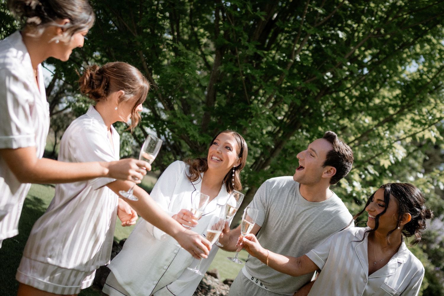 A group dressed in white shares drinks and laughter together during a sunny outdoor gathering.