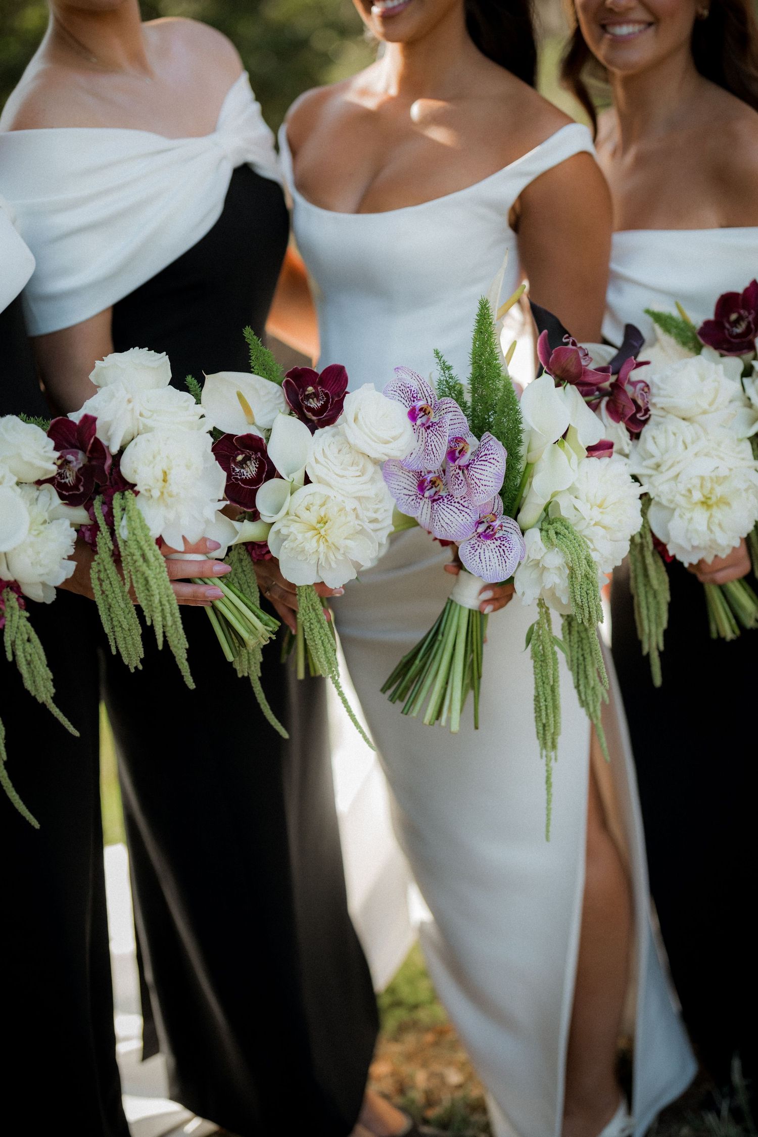 Row of elegant white and burgundy wedding bouquets held by bridesmaids.