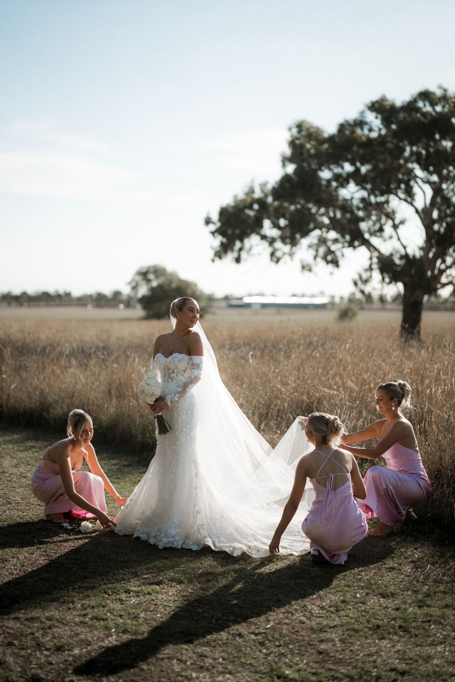 Wedding party relaxing in a golden field during sunset with flowing dresses creating beautiful silhouettes.