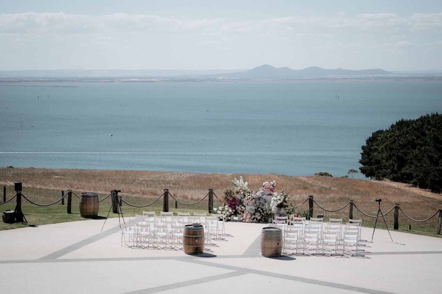 A scenic outdoor wedding ceremony setup overlooking mountains and ocean views on a sunny day.