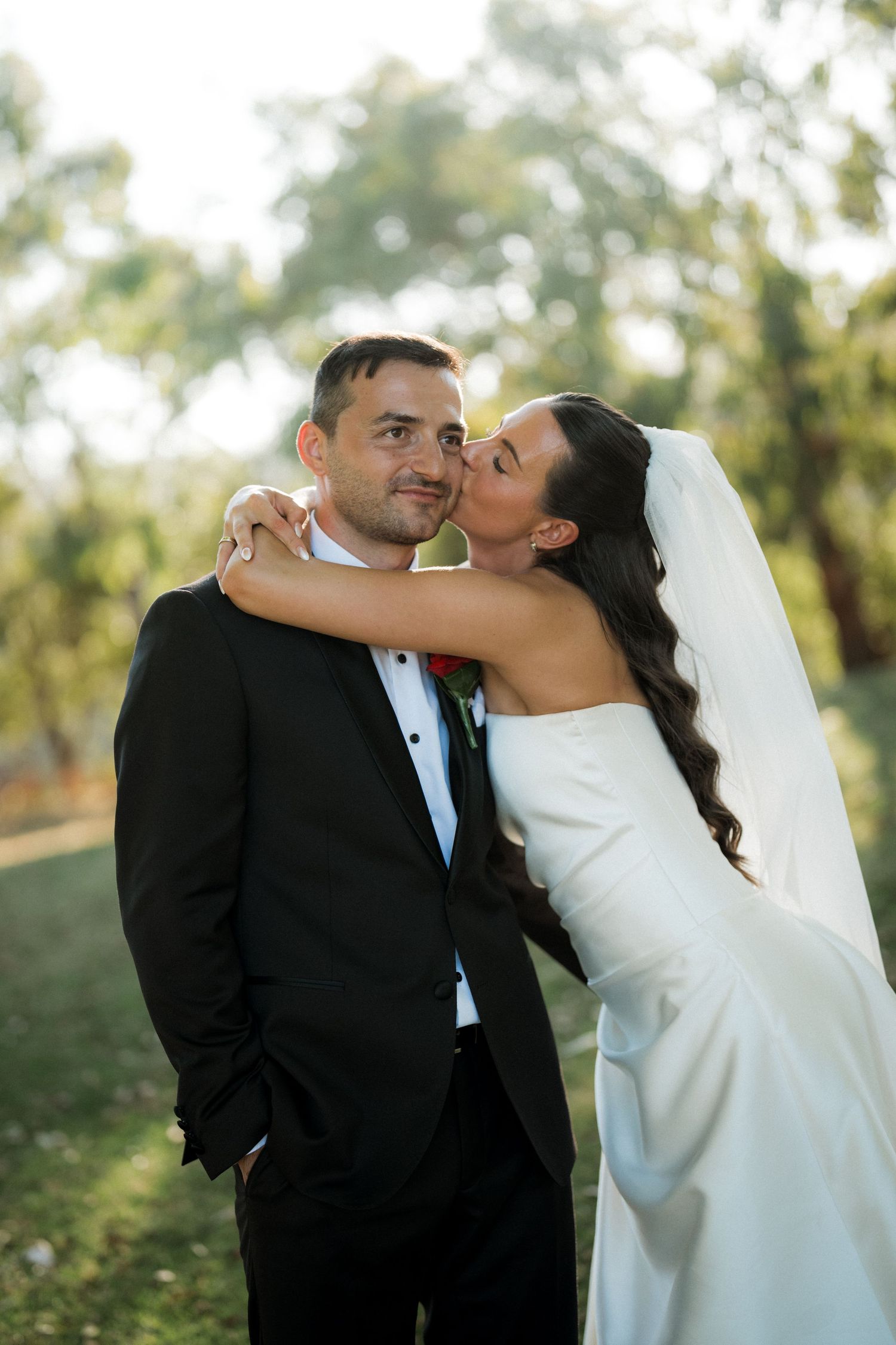 Romantic wedding couple embracing outdoors in formal attire during sunset photoshoot.