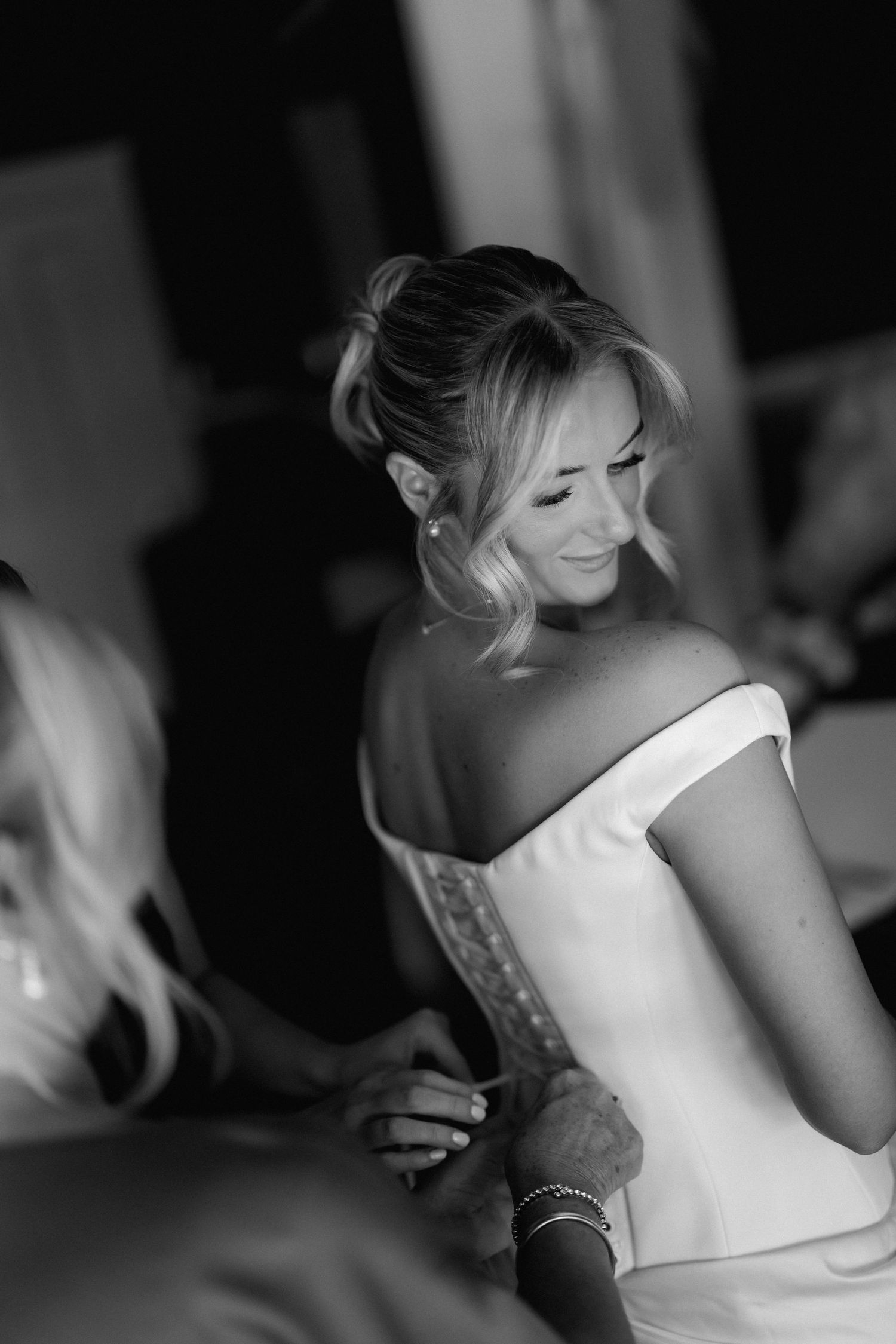 A series of black and white photos showing the back of a bride in a white wedding dress getting ready for her ceremony.