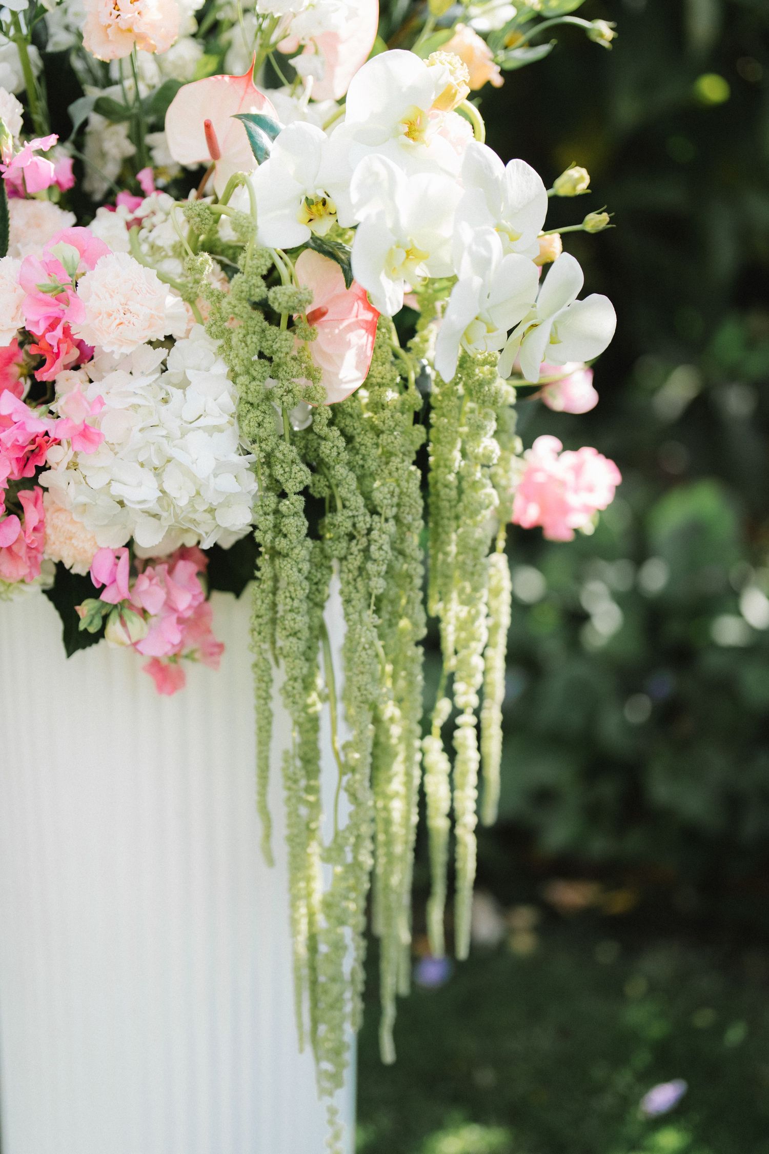 Elegant floral wedding arch arrangement with cascading white and pink flowers against a dark green background.