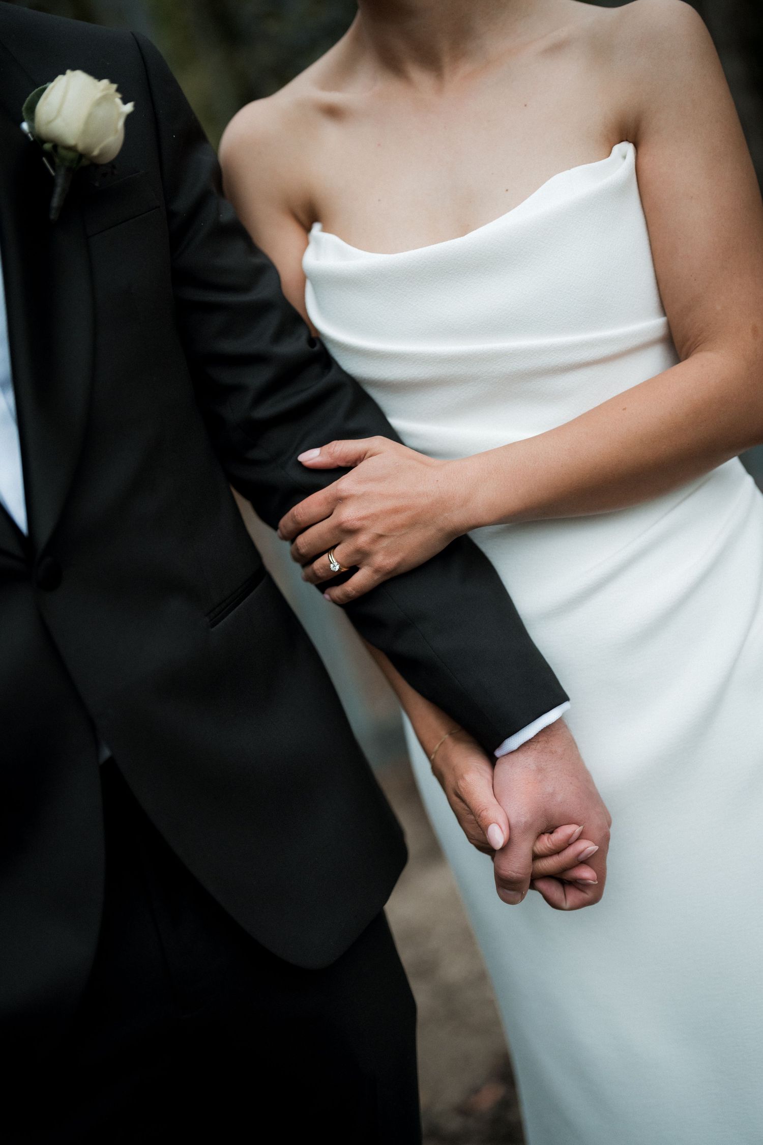 Close-up detail of formal wedding attire showing white dress and black tuxedo with hands clasped.