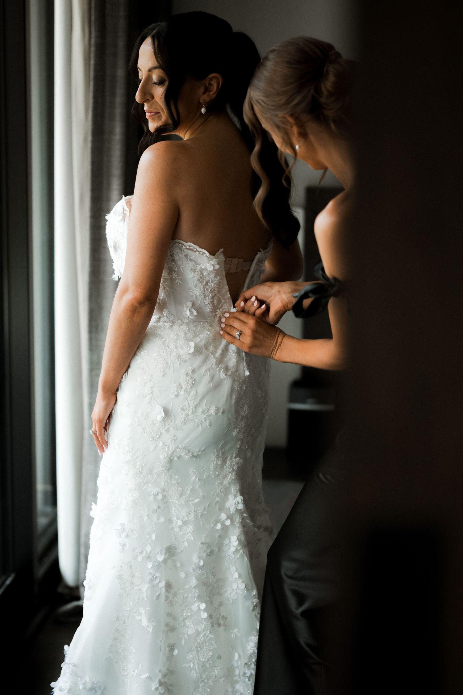 Detail shots of a white lace wedding dress being adjusted in natural window light.