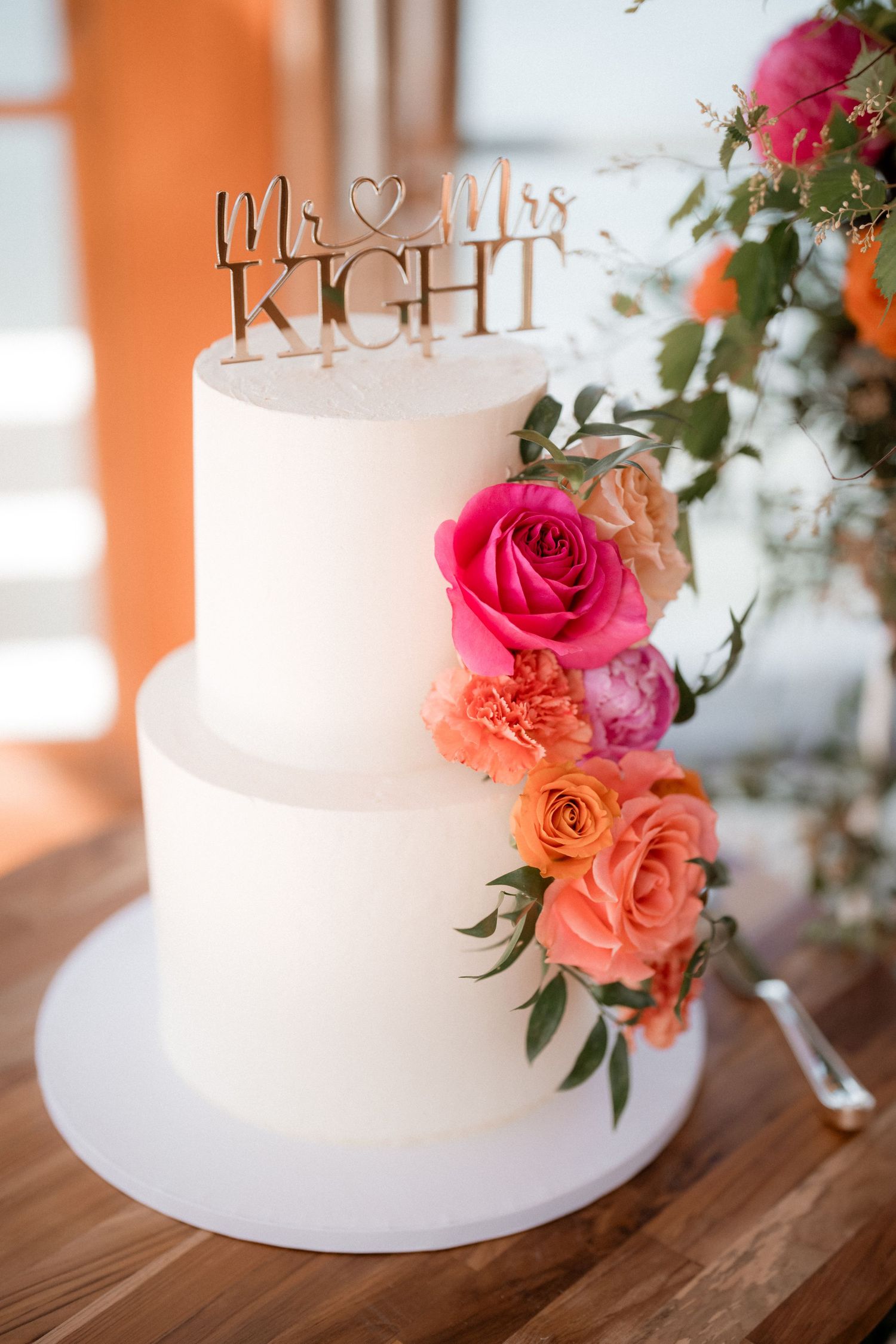 Elegant two-tier white wedding cake decorated with cascading pink and coral roses and a 'Mr & Mrs Right' cake topper.