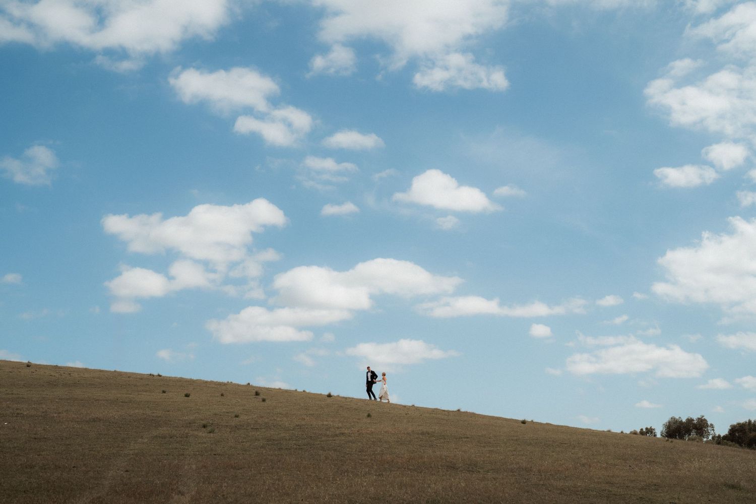 A lone hiker stands silhouetted against a cloudy blue sky on a grassy hilltop.