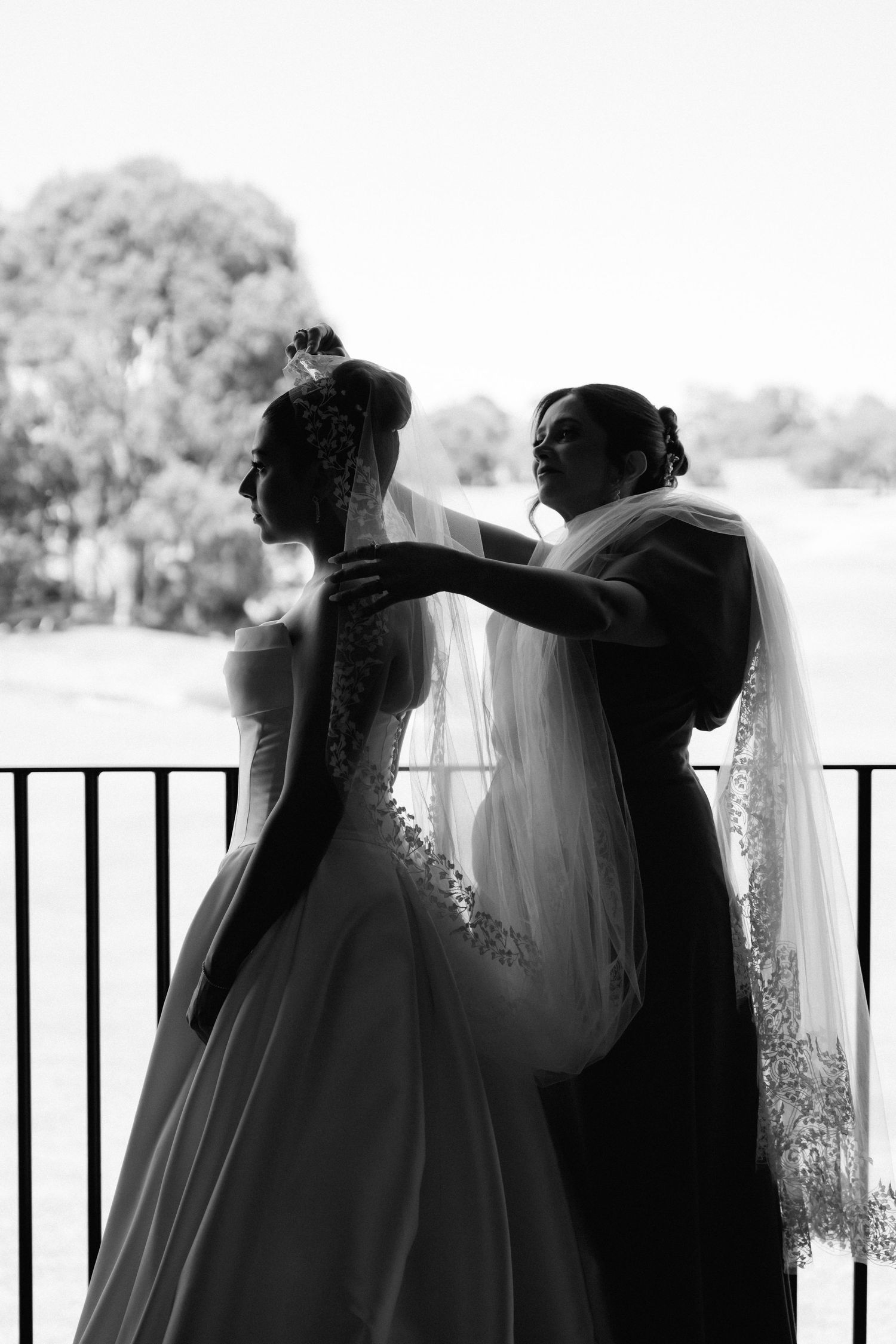 Silhouetted couple embraces on a balcony with iron railings in dramatic black and white photography.