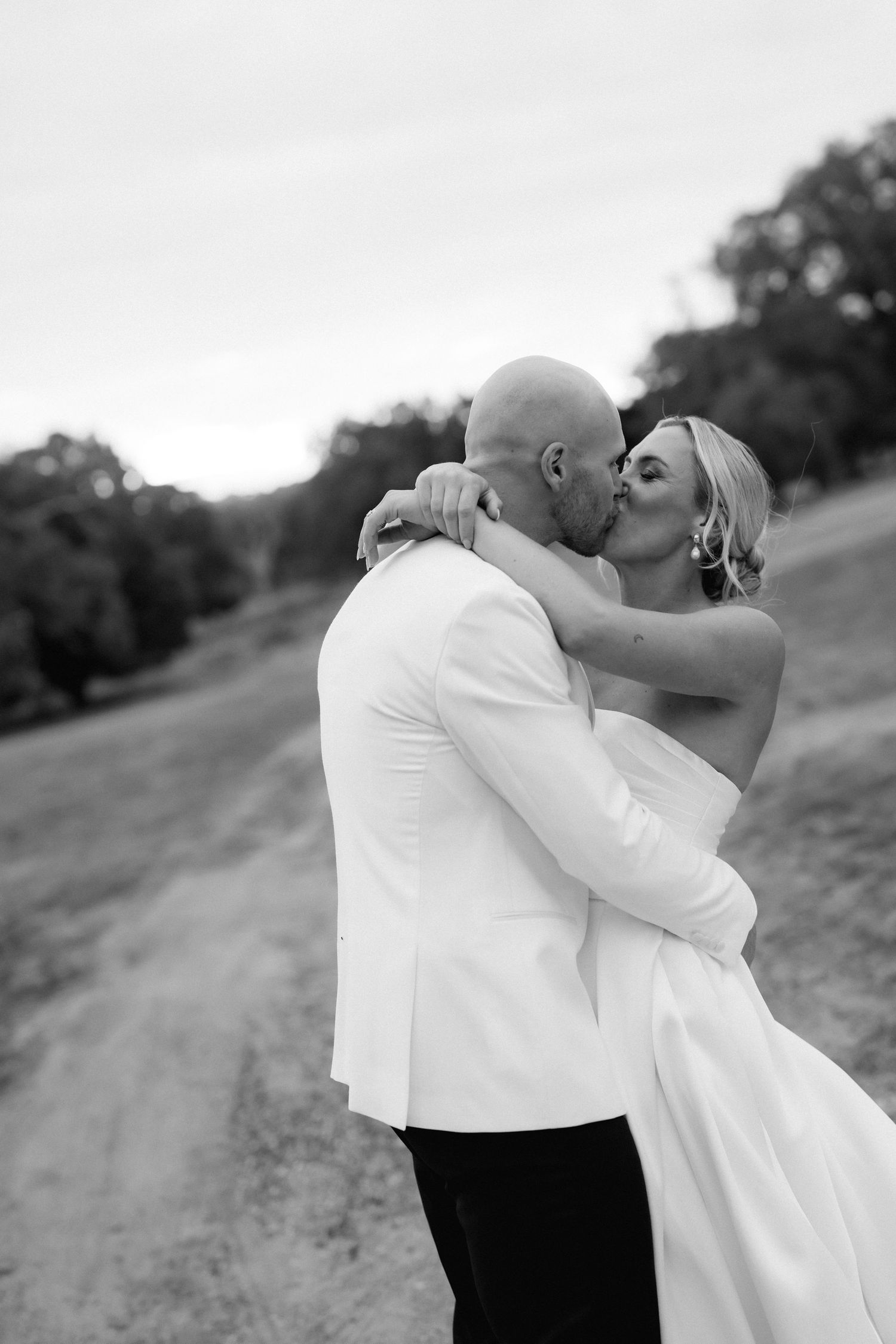 A romantic black and white portrait capturing a tender moment between newlyweds on a country road.