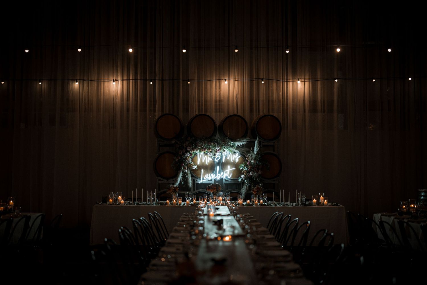 Elegant wedding reception table setup with dramatic lighting and glowing display at the end of a dark banquet hall.