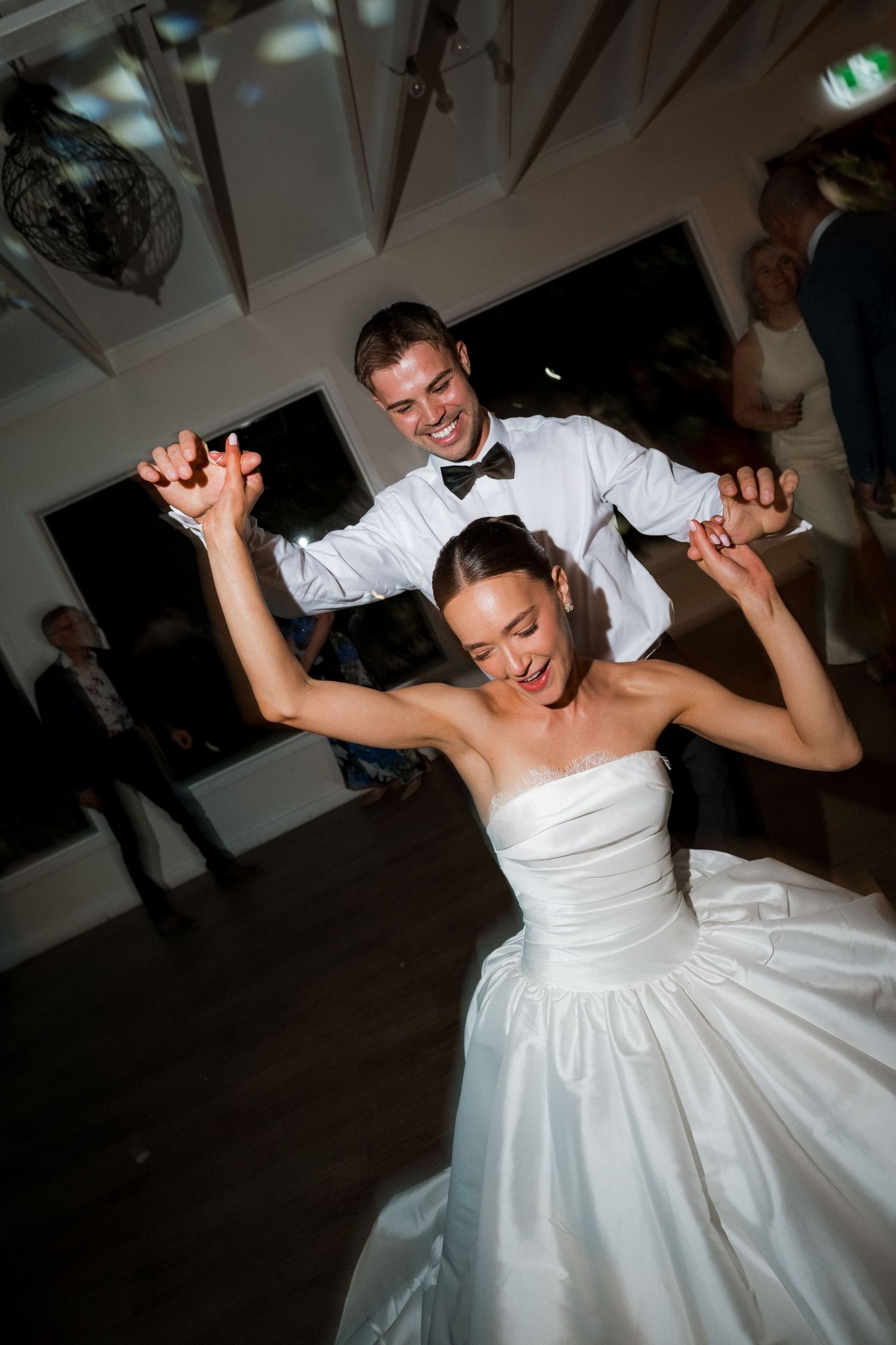 A couple dances energetically at their wedding reception in formal attire.